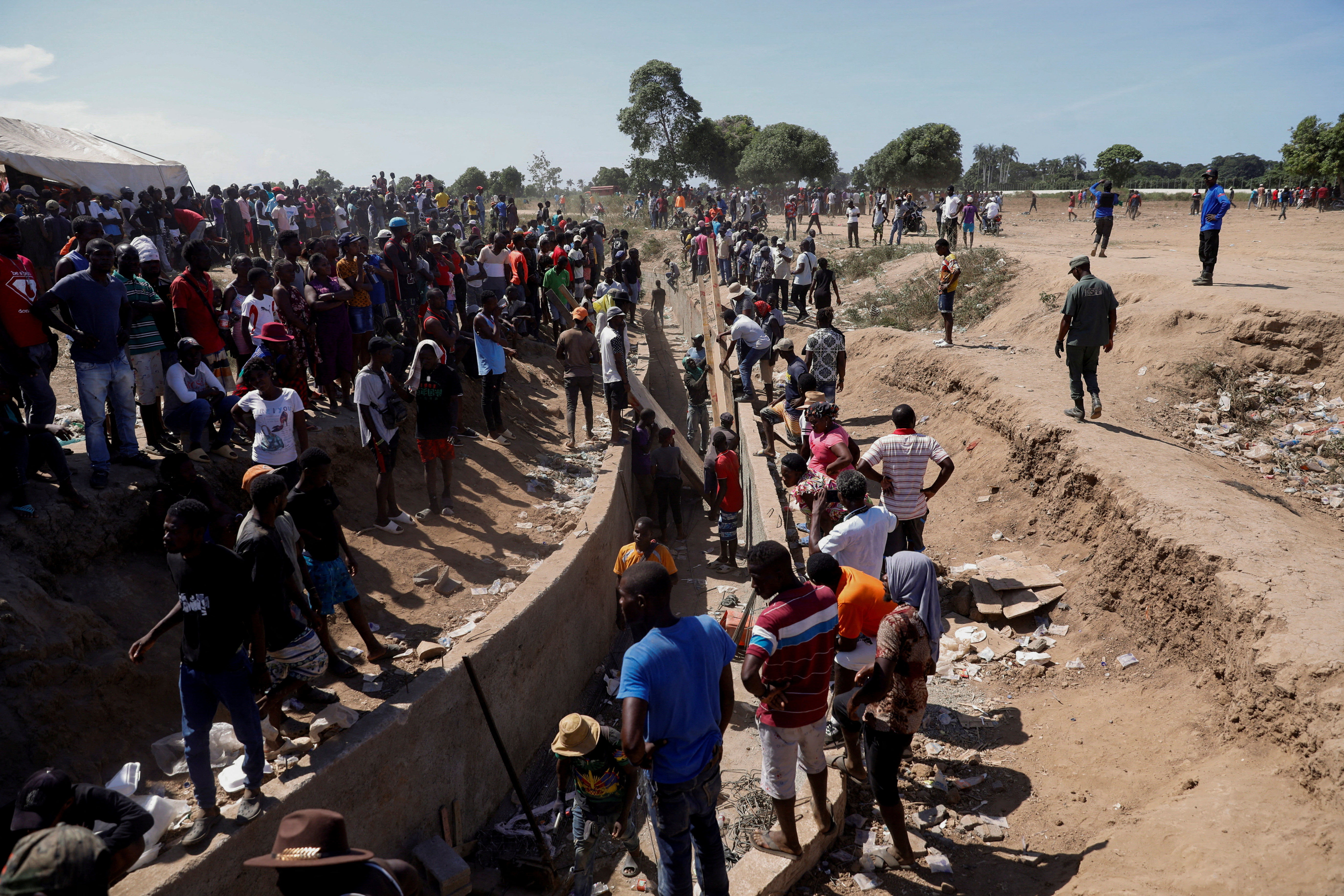 Haitians work on the construction site of a water channel from the Massacre river, a river shared between Haiti and the Dominican Republic, after Dominican President Luis Abinader announced a total border shutdown amid a conflict over the construction of the channel, in Ouanaminthe, Haiti September 15, 2023. Seen from above, the canal workers are numerous. They shape a curved pathway through the brown dirt for water to eventually flow.