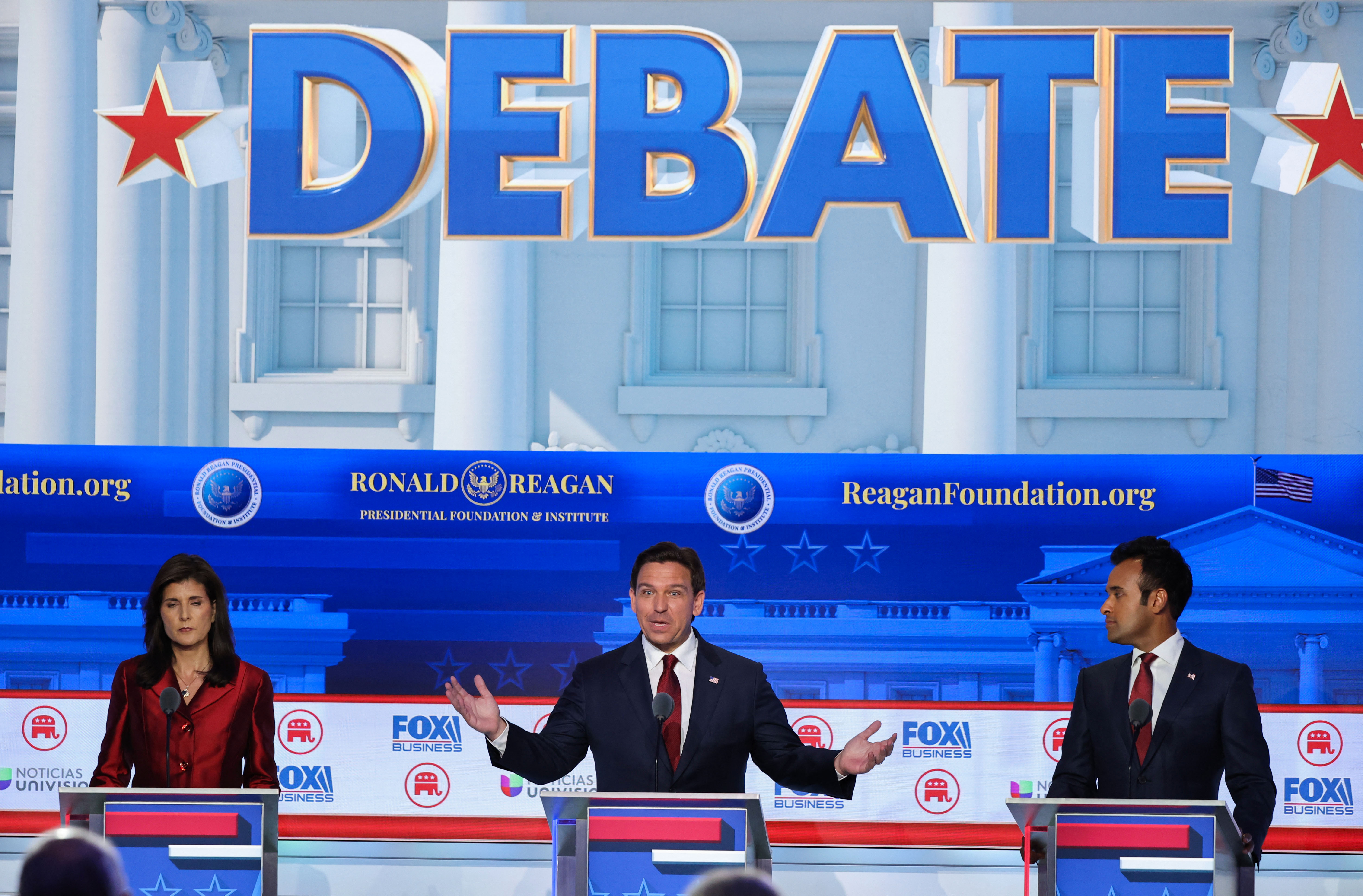 Three of the Republican candidates on stage during the debate. Ron DeSantis is in the centre with his hands out making a point. On his right is Nikki Haley on his left Vivek Ramaswamy