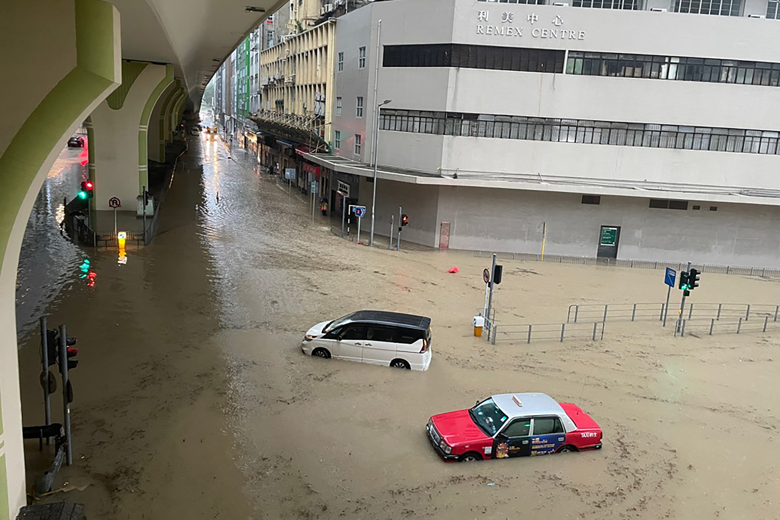 Stranded vehicles on a flooded road junction in Hong Kong. There is a flyover to the left and buildings behind. The water is milky brown.