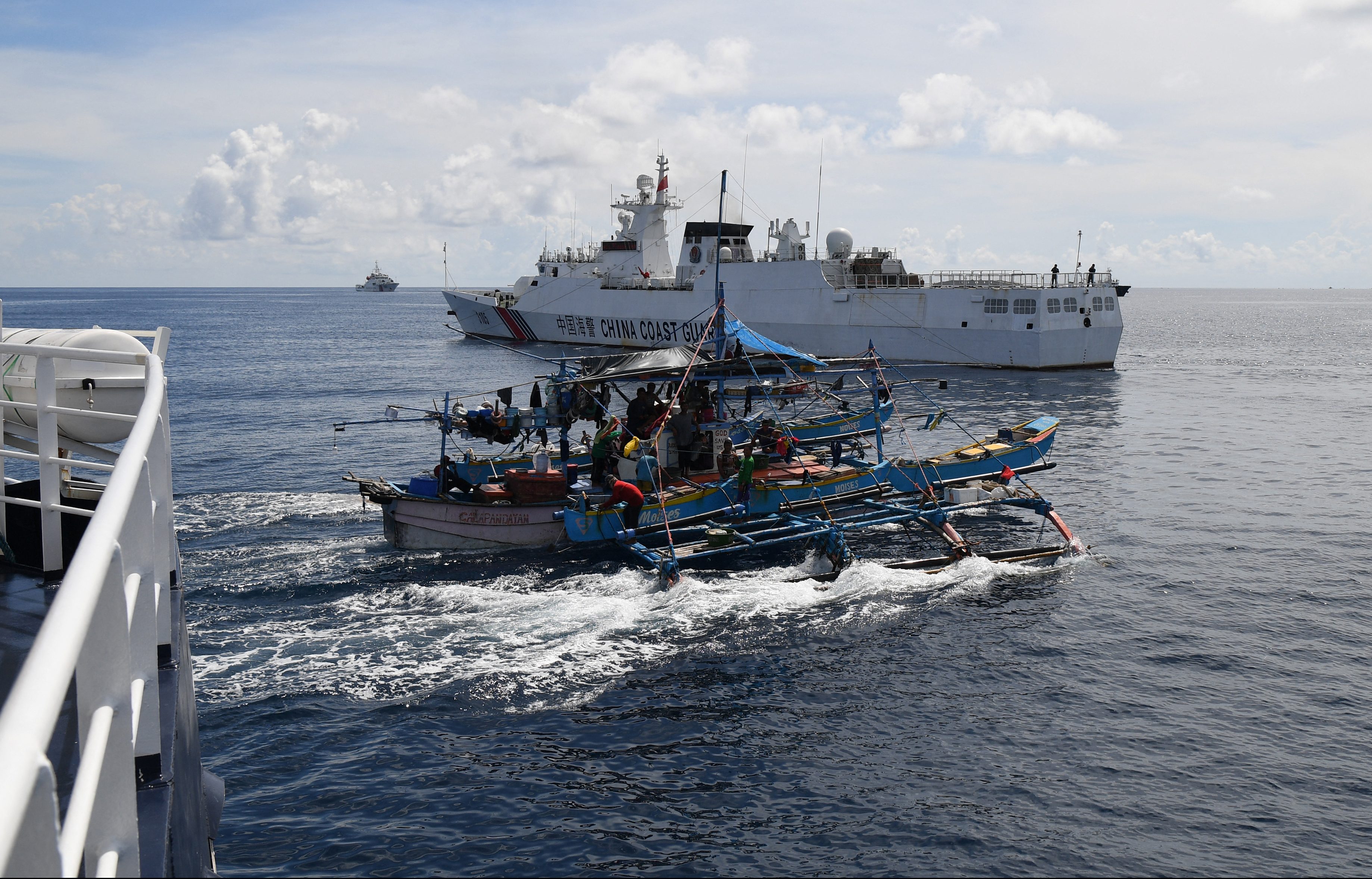This photo taken on September 22, 2023 shows Philippine fishing motherboat "Moises" (C) sailing past a Chinese coast guard ship (background) after the former was blocked from sailing near the Chinese-controlled Scarborough Shoal in disputed waters of the South China Sea. China, which claims sovereignty over almost the entire South China Sea, snatched control of Scarborough Shoal from the Philippines in 2012. Since then, it has deployed coast guard and other vessels to block or restrict access to the fishing ground that has been tapped by generations of Filipinos. (Photo by Ted ALJIBE / AFP)