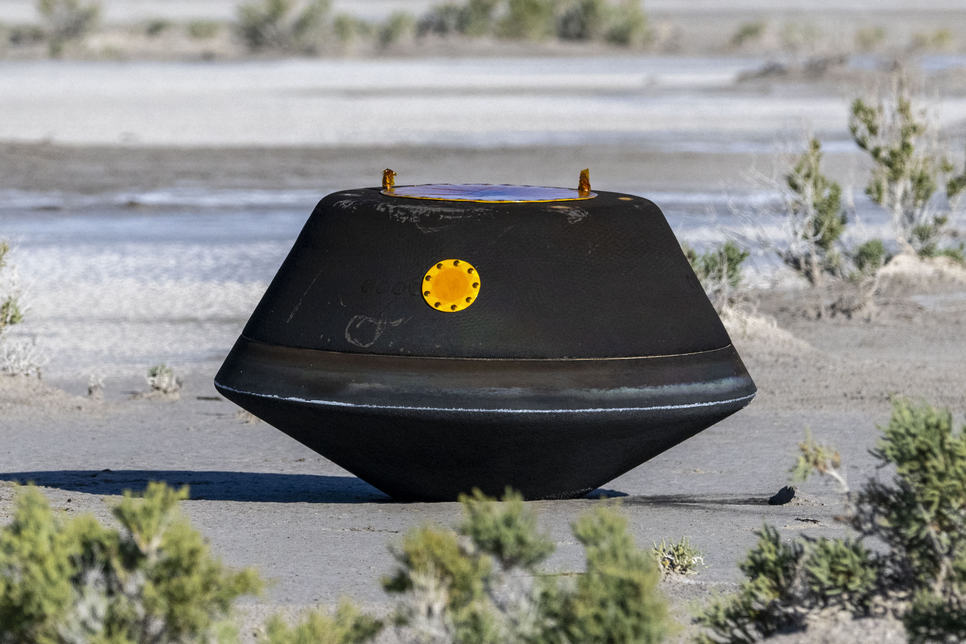 The capsule containing the asteroid samples in the desert. It is black and shaped a like a lozenge.