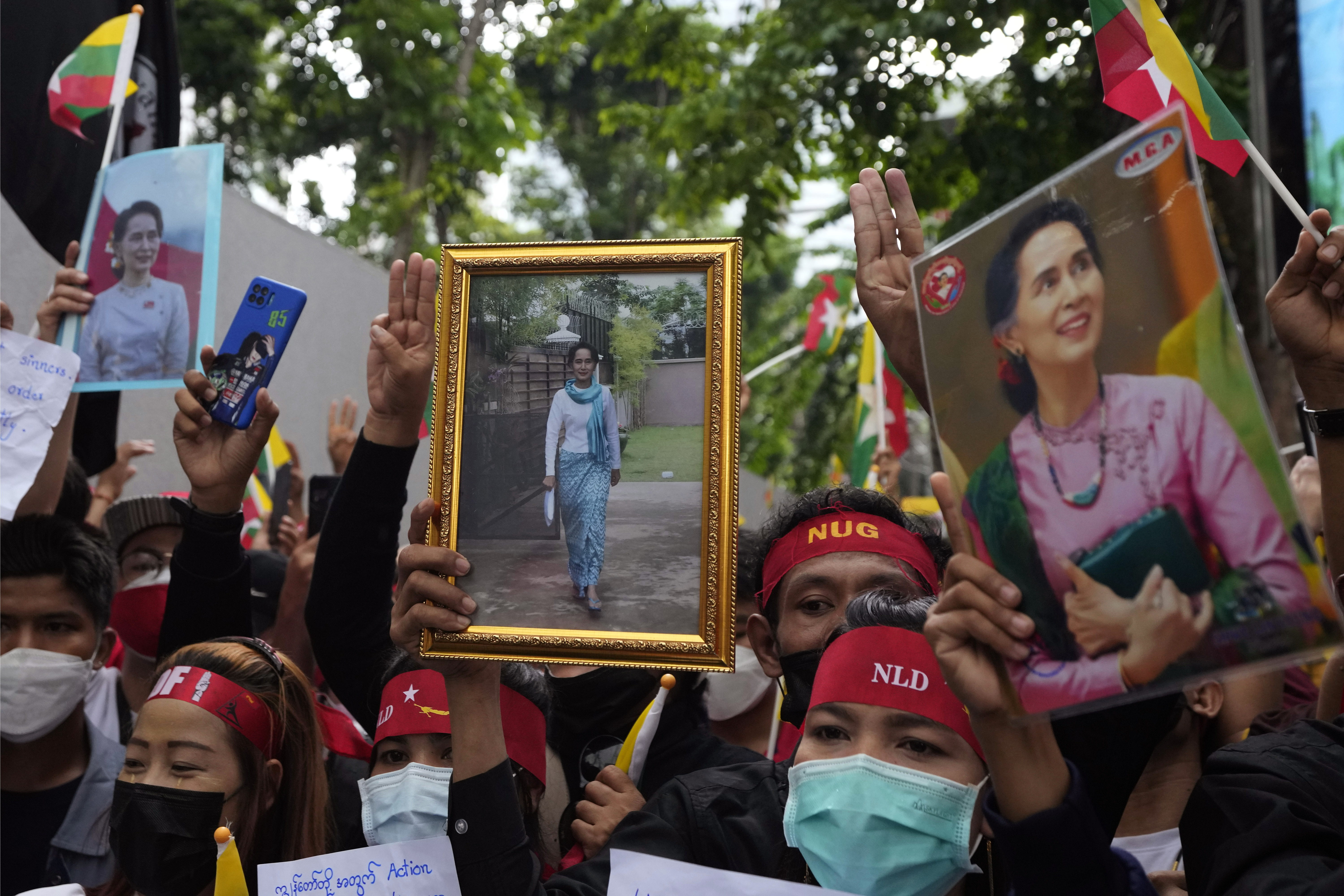 Protesters in Bangkok march with pictures of Aung San Suu Kyi. They are wearing red bandanas with NLD written in white. Some are making the three fingered salute