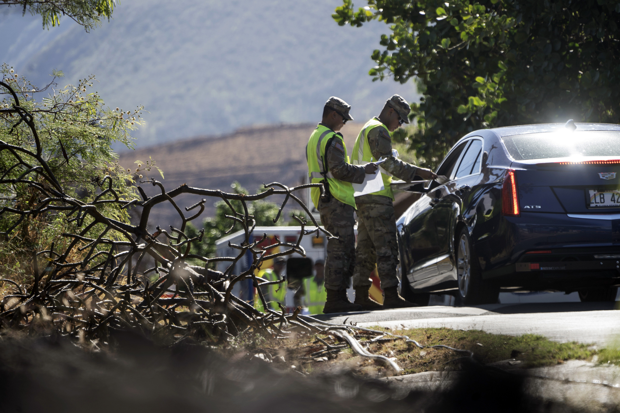 Two people in yellow traffic vests stand outside of a car and speak to the driver through the open window.