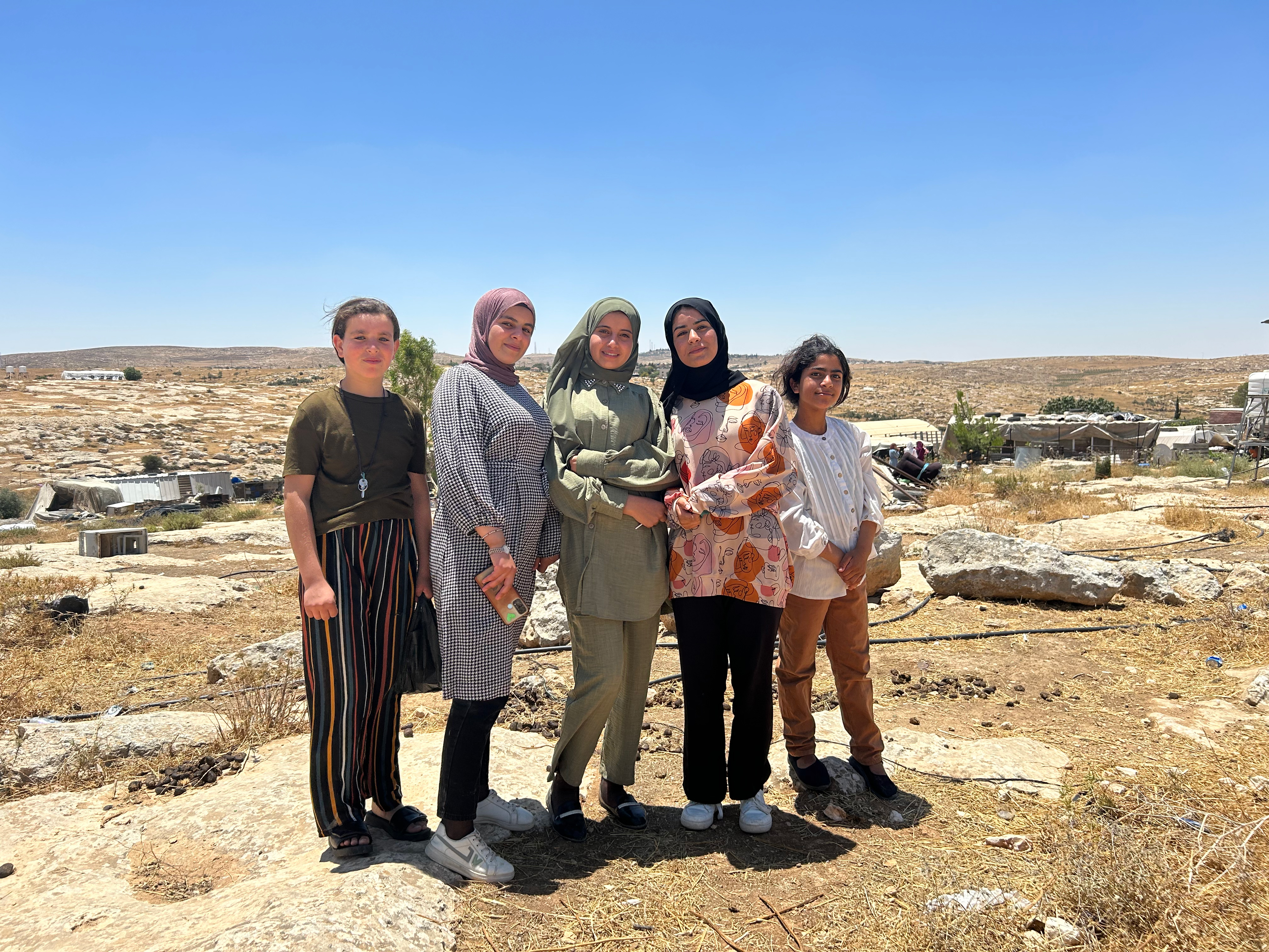 Five young girls who just finished playing on Khirbet Susiya’s playground stand triumphantly in front of their village.