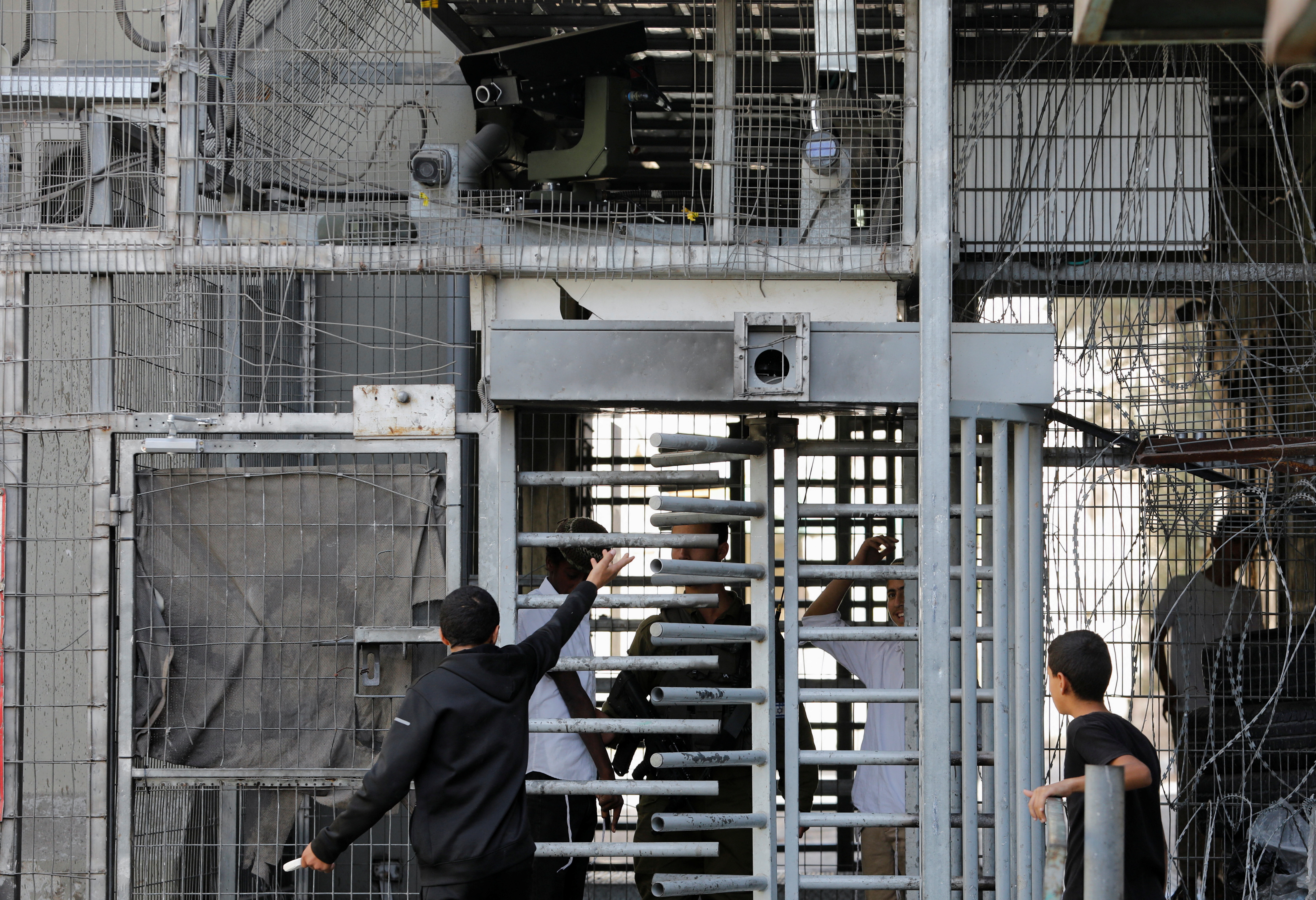 A Palestinian youth argues with Israeli settlers as a remote-controlled gun is seen on an Israeli army checkpoint in Hebron, in the Israeli-occupied West Bank September 26, 2022. REUTERS/Mussa Qawasma