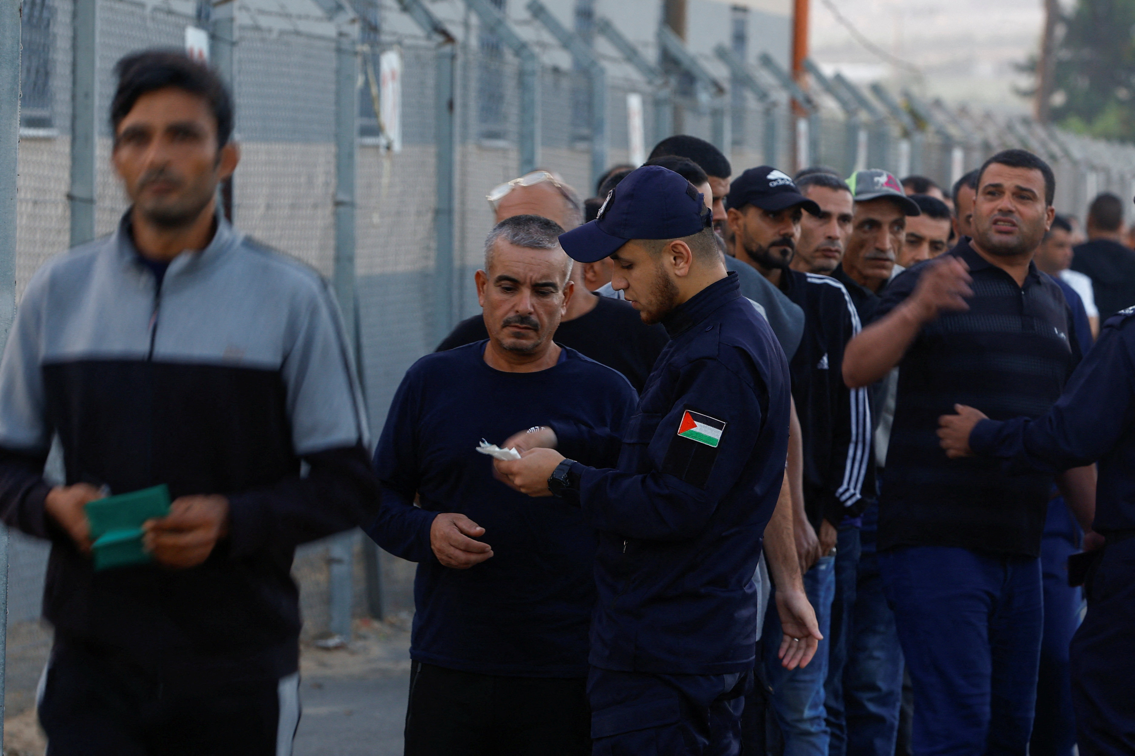 A Palestinian police officer checks the documents of Palestinian workers as they enter the Beit Hanoon (Erez) crossing to Israel, September 28, 2023 [Ibraheem Abu Mustafa/Reuters]