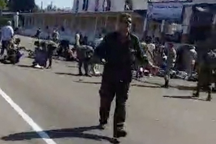 People stand and walk outside a building after drone attack on Syrian military academy in Homs, Syria