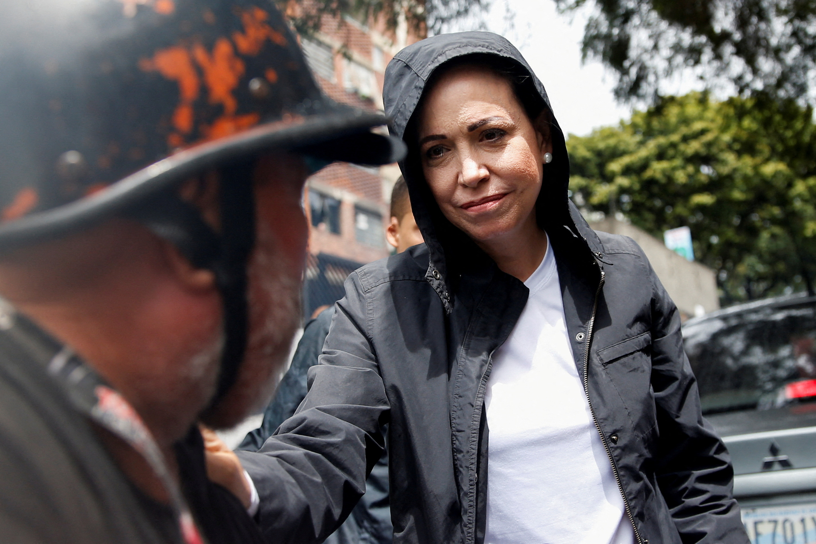 A woman in a grey hoodie reaches out and puts a hand on the shoulder of a man looking toward her.