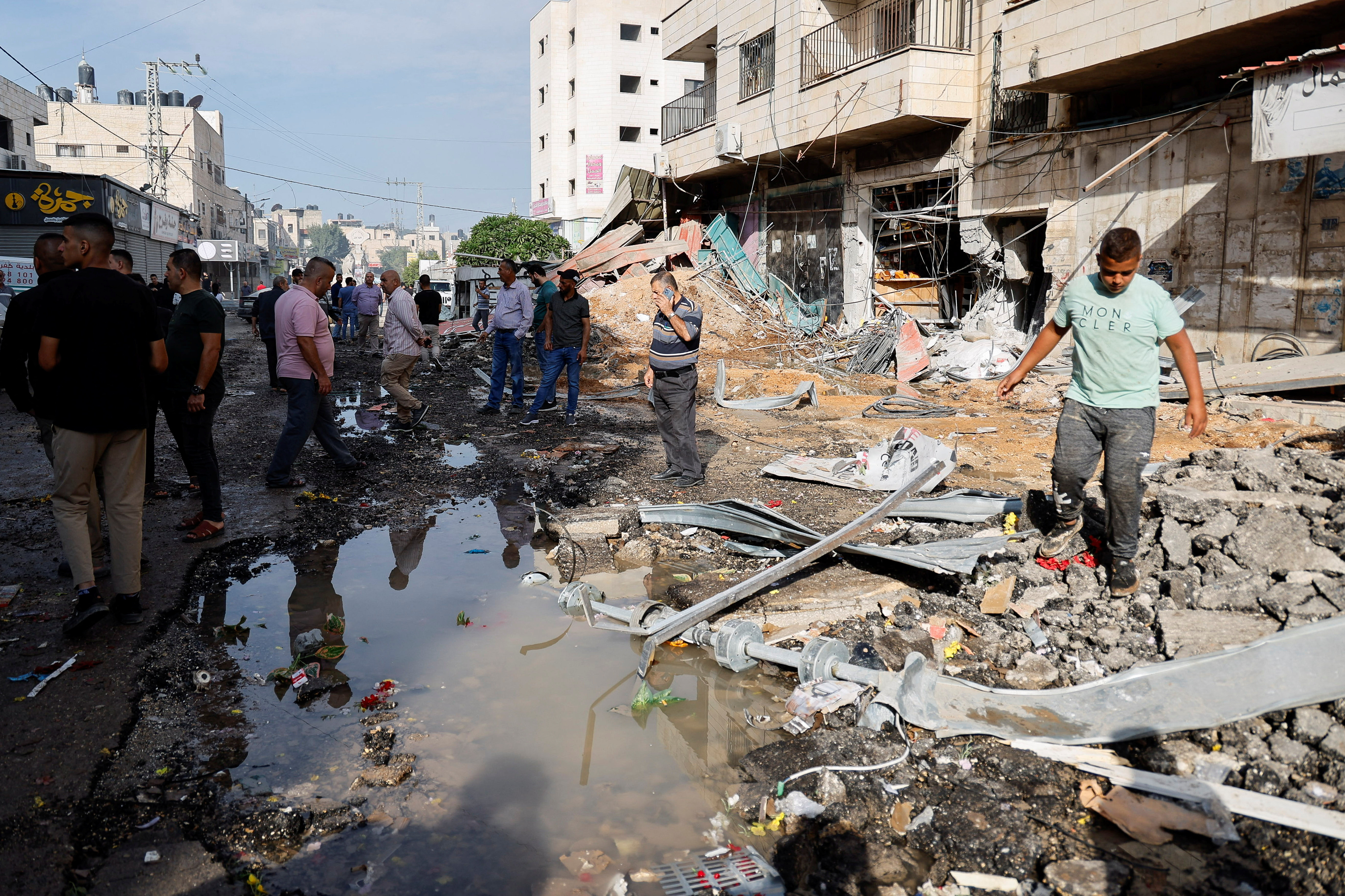 Palestinians stand on a damaged street, following an Israeli raid in Jenin,