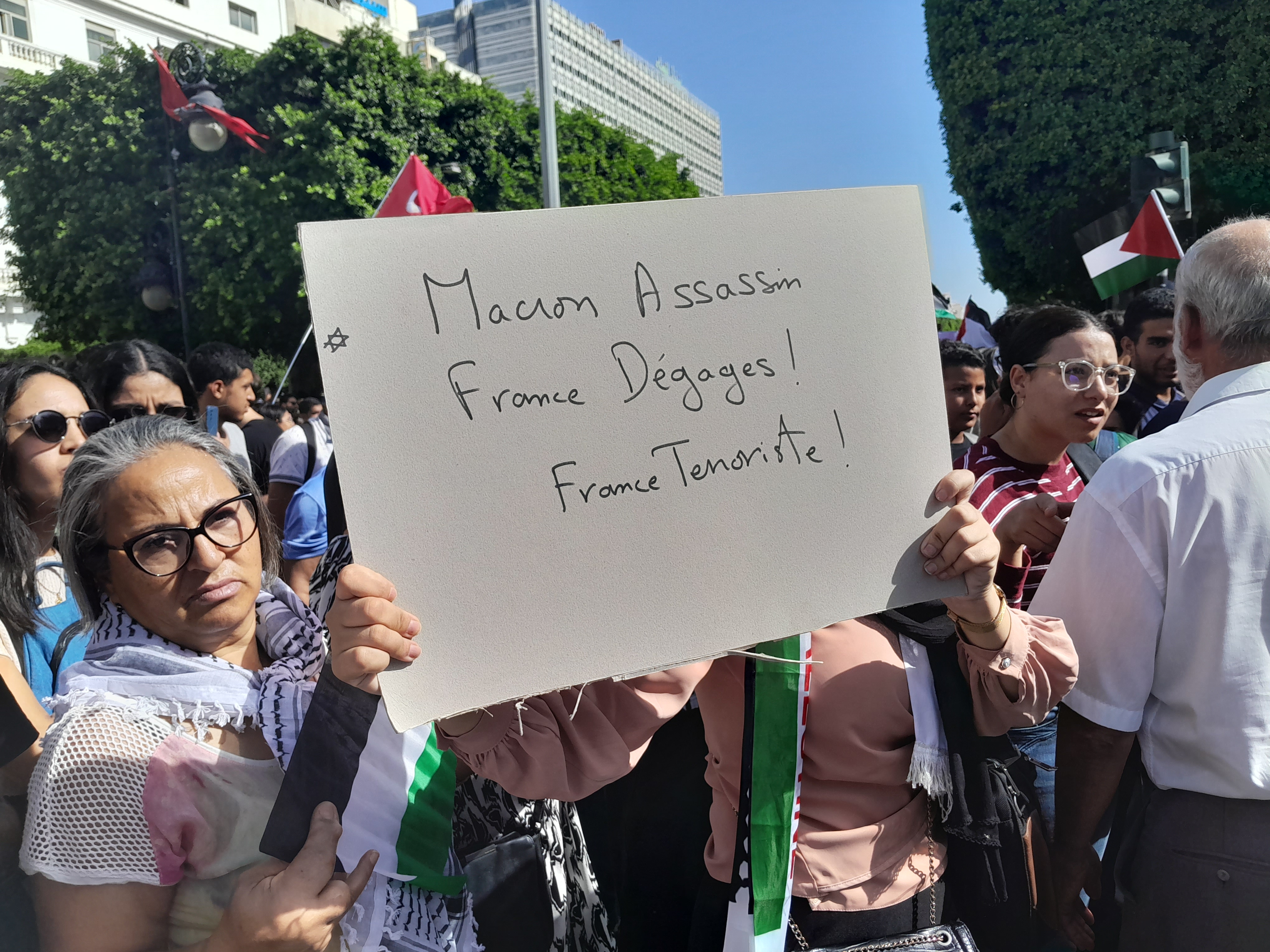 A protester holds up a handwritten sign that reads, "Macron assassin. France, dégages! France terroriste."