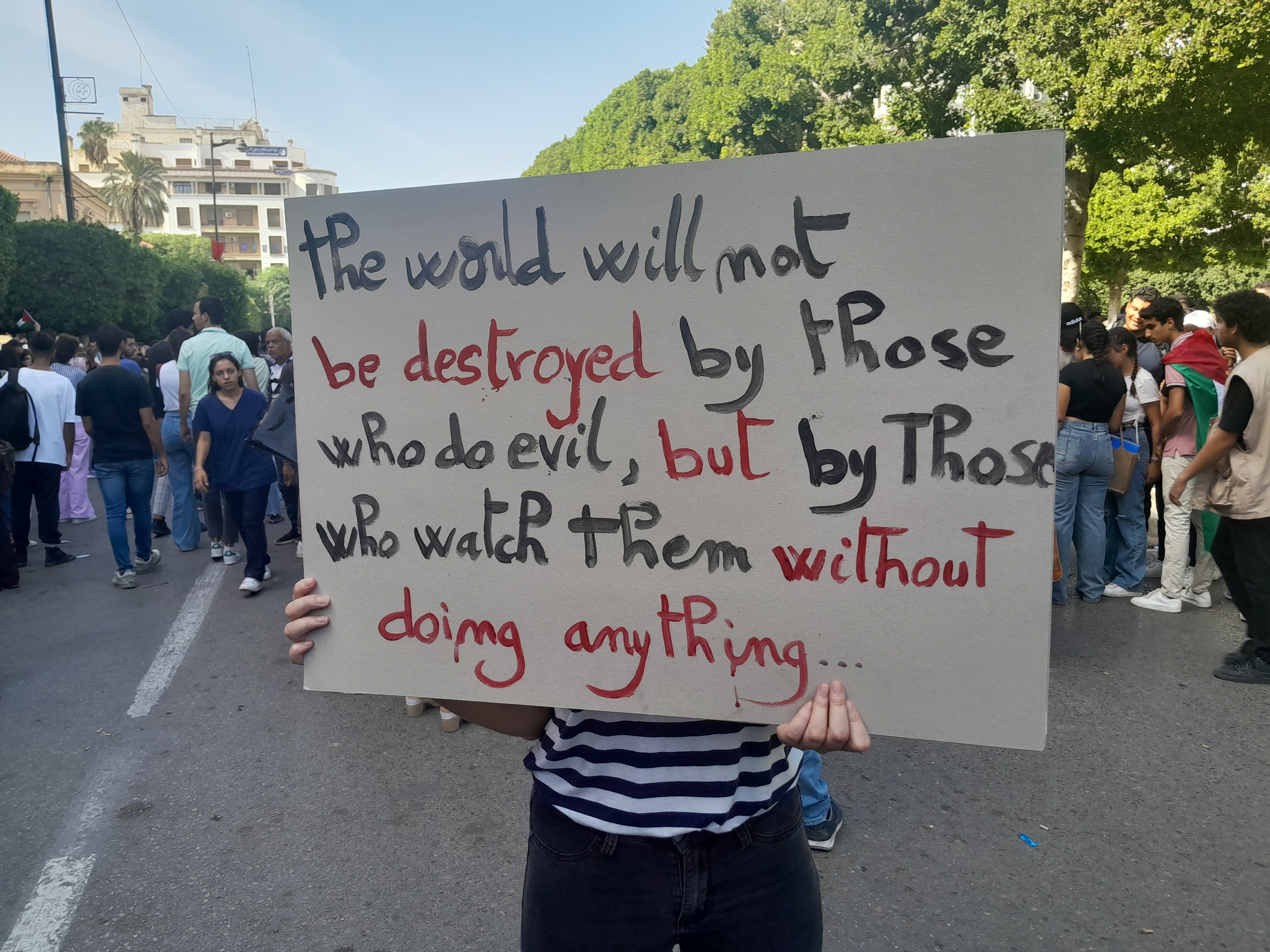 A protester in Tunis holds up a handmade sign that reads, "The world will not be destroyed by those who do evil but by those who watch them without doing anything."