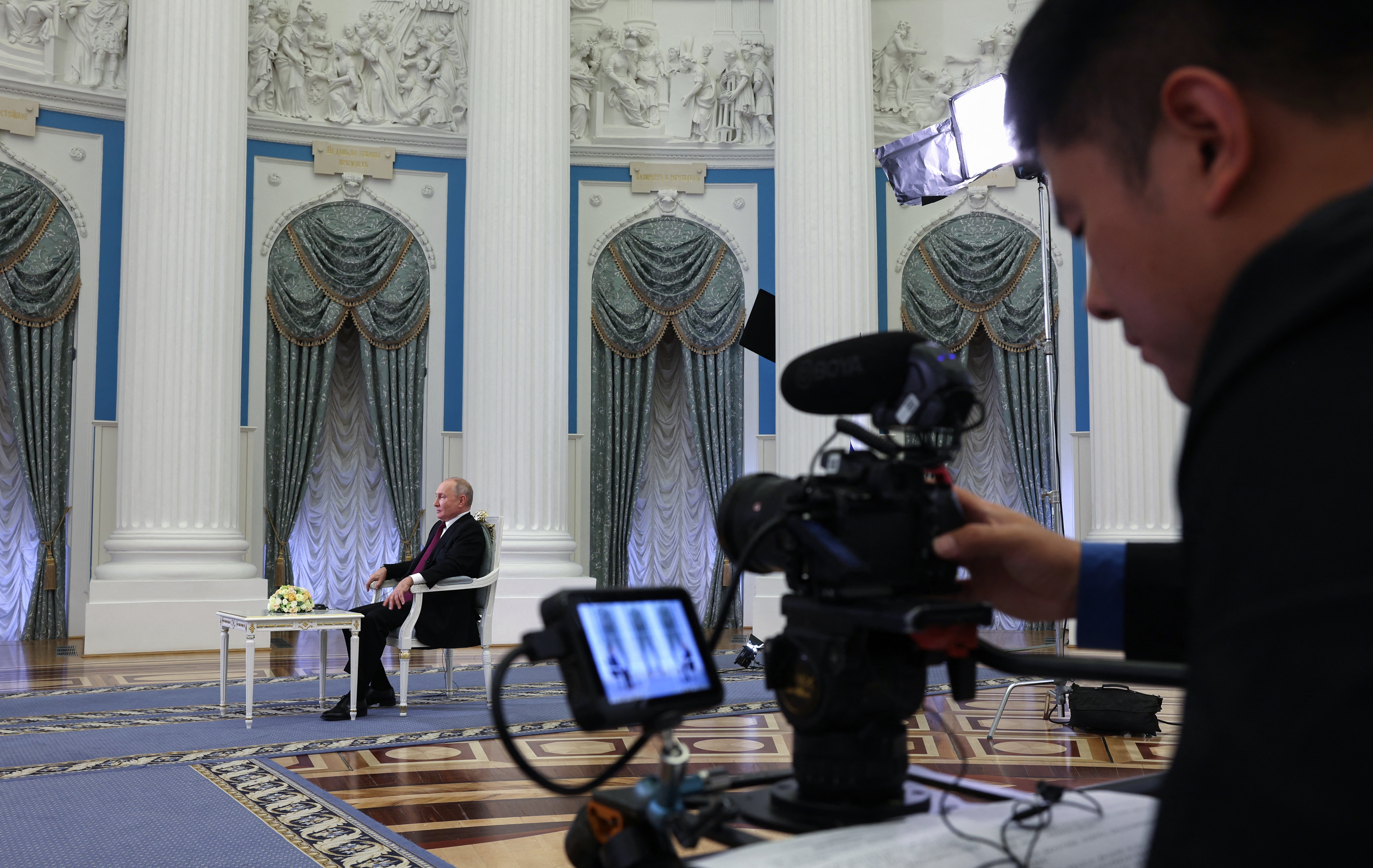 Putin being interviewed in Moscow by Chinese state media at the Kremlin. He is in cavernous white and blue coloured room. 