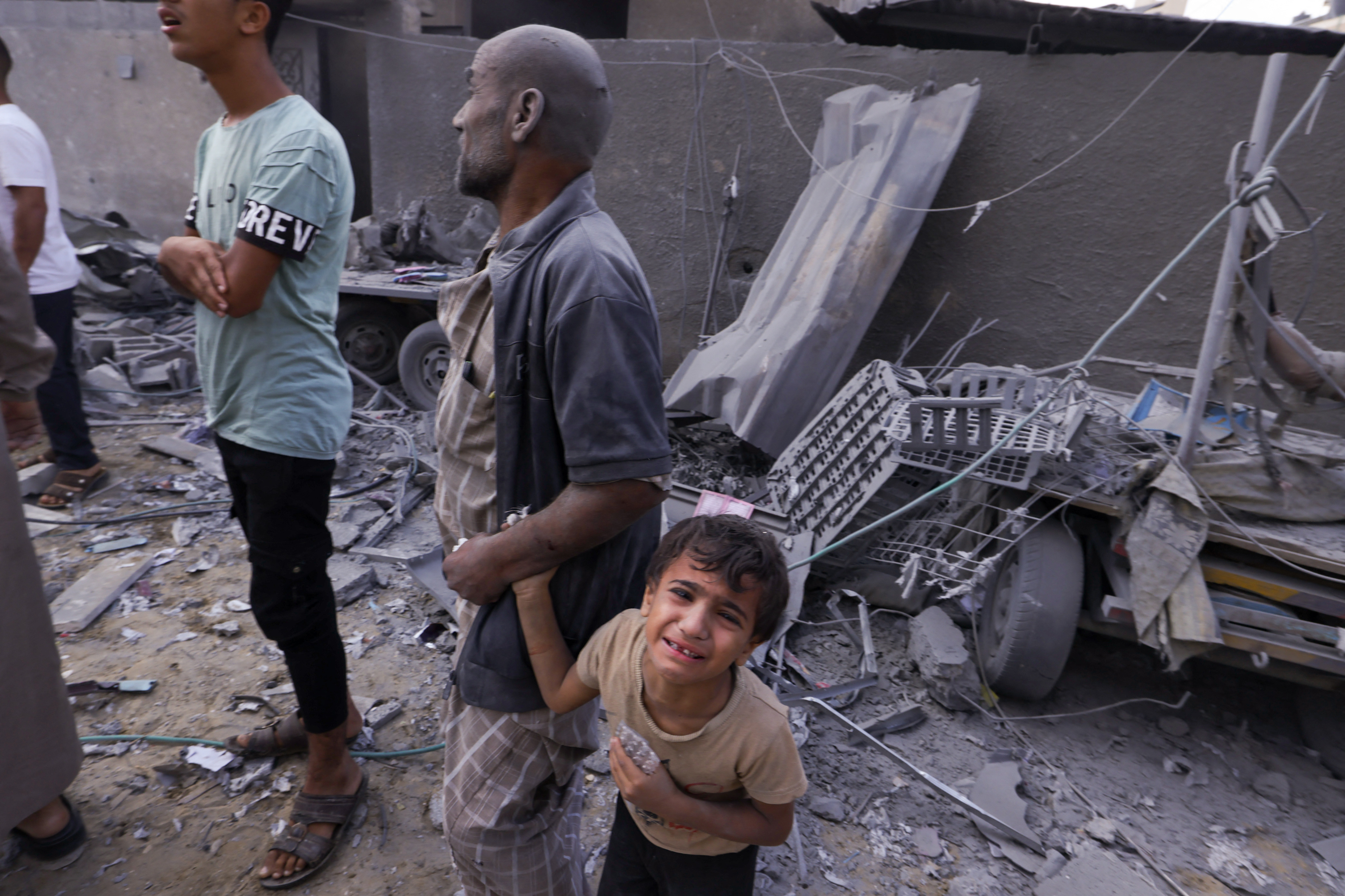 A Palestinian man covered in dust holds the hand of a weeping child following an Israeli airstrike on Rafah, in the southern Gaza Strip on October 17, 2023 [Mohammed Abed/ AFP]