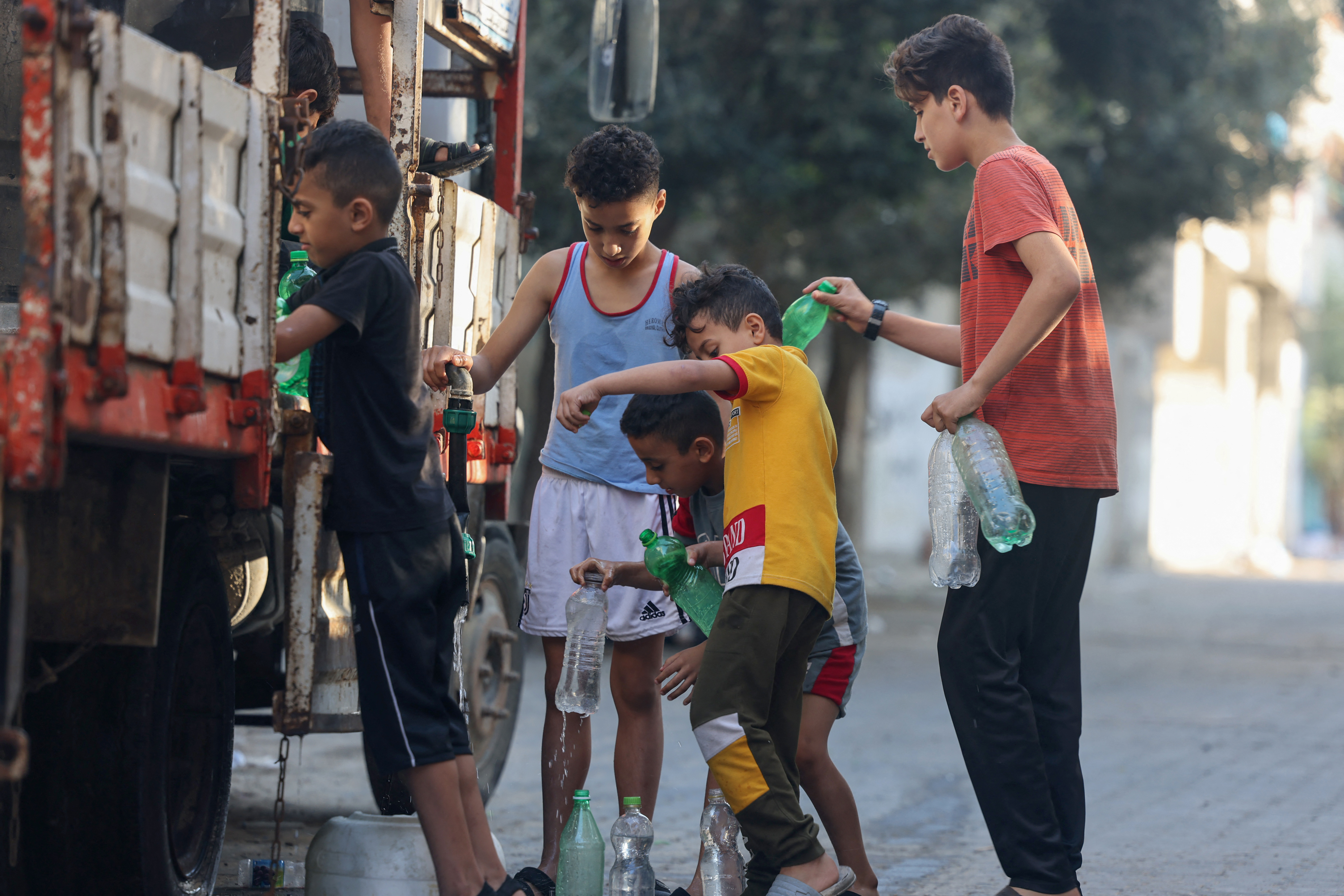 Children queue to fill bottles of water to last them until their next refill, possibly days later
