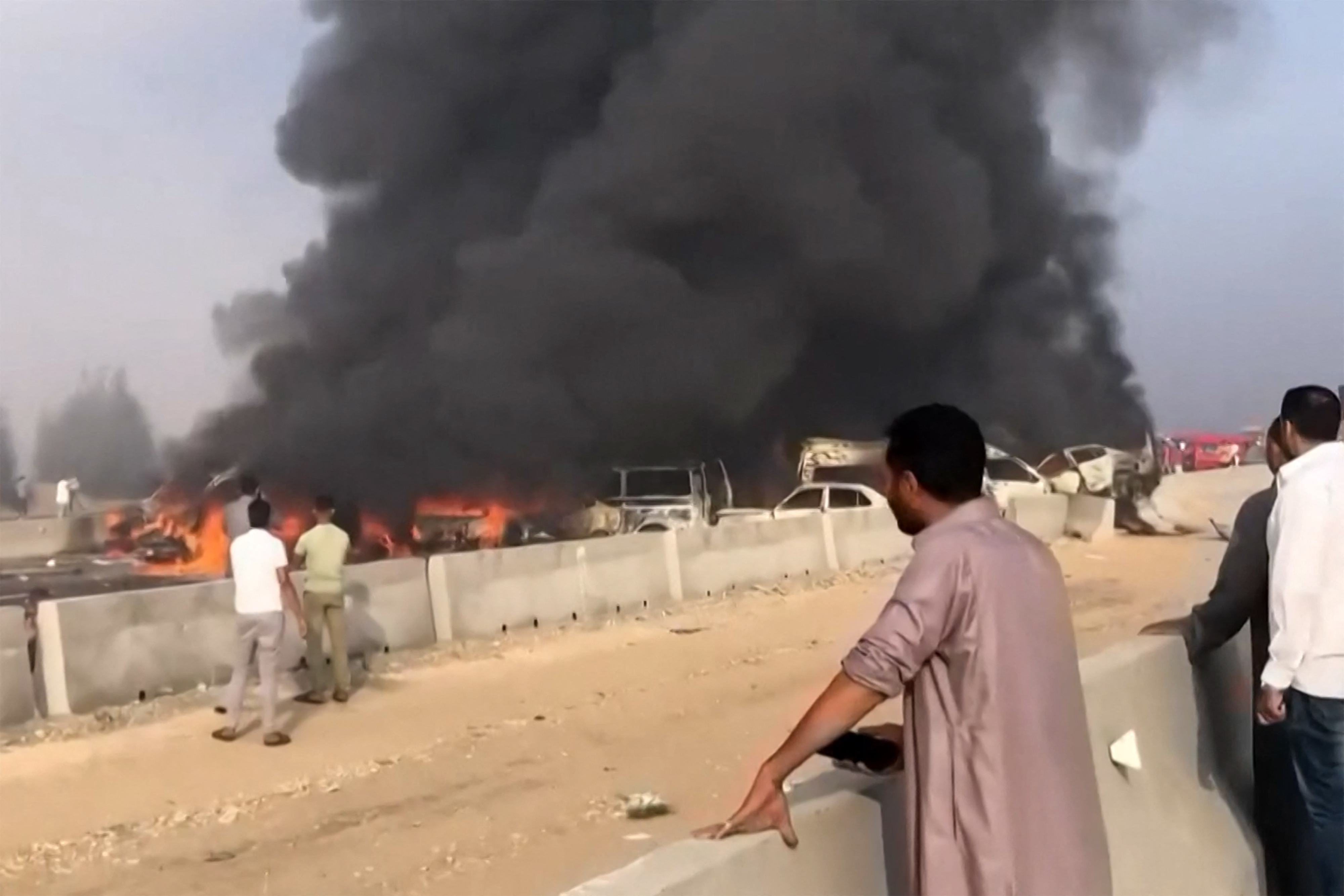 A grab from a UGC video posted on Facebook on October 28, 2023, shows people watching as black smoke billows from charred vehicles following a collision on the Cairo-Alexandria desert road near Wadi al-Natrun that reportedly left at least 35 people dead and more than 50 people dead. - Traffic accidents are common in Egypt where roads are often in bad repair and the highway code is frequently disregarded. (Photo by -UGC / UGC / AFP) / RESTRICTED TO EDITORIAL USE MANDATORY CREDIT « AFP PHOTO / UGC VIA FACEBOOK» - NO MARKETING NO ADVERTISING CAMPAIGNS NO RESALE DISTRIBUTED AS A SERVICE TO CLIENTS - RESTRICTED TO EDITORIAL USE MANDATORY CREDIT « AFP PHOTO / UGC via Facebook» - NO MARKETING NO ADVERTISING CAMPAIGNS NO RESALE DISTRIBUTED AS A SERVICE TO CLIENTS /