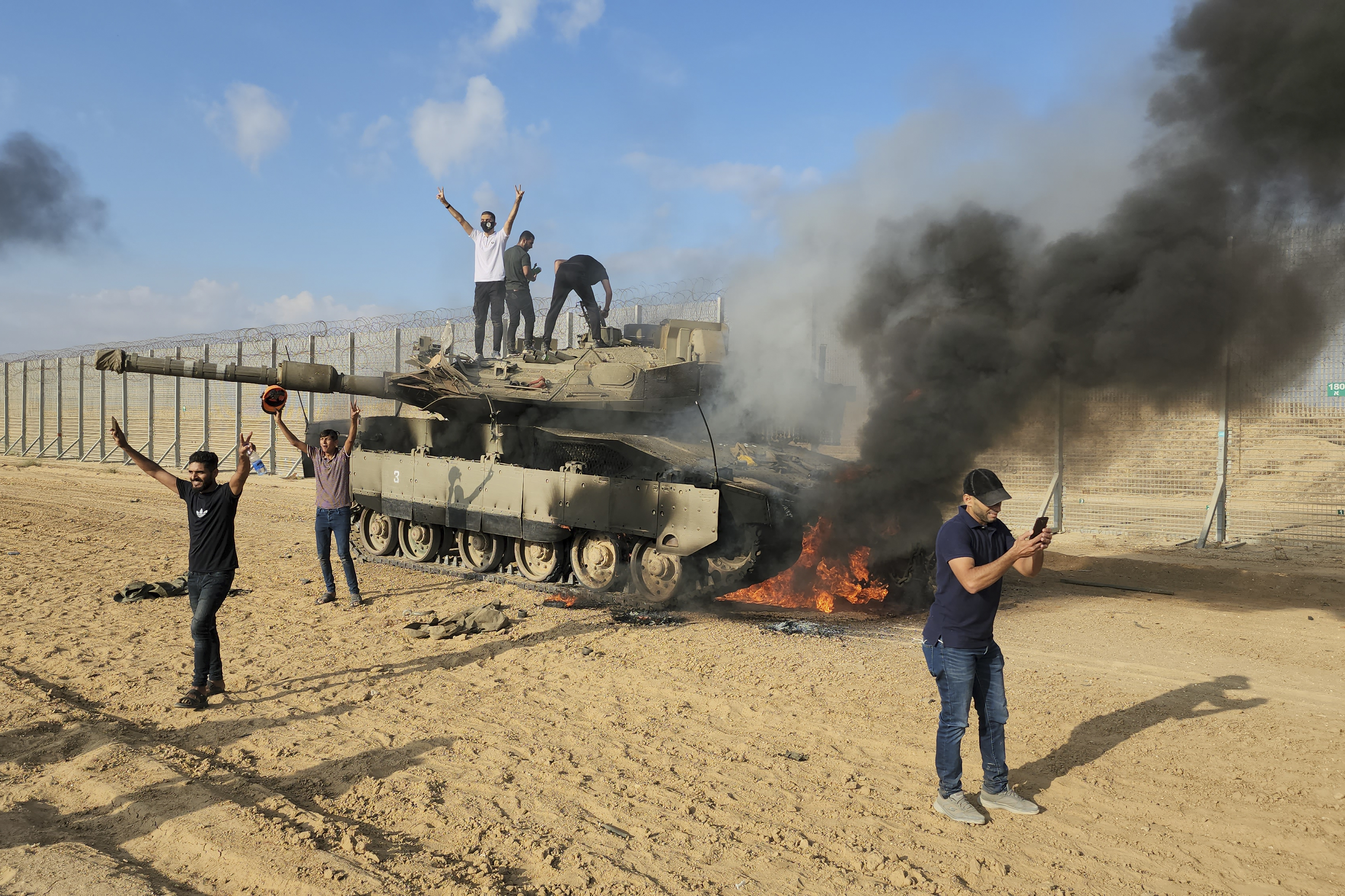 Palestinians celebrate by a destroyed Israeli tank at the Gaza Strip fence east of Khan Younis