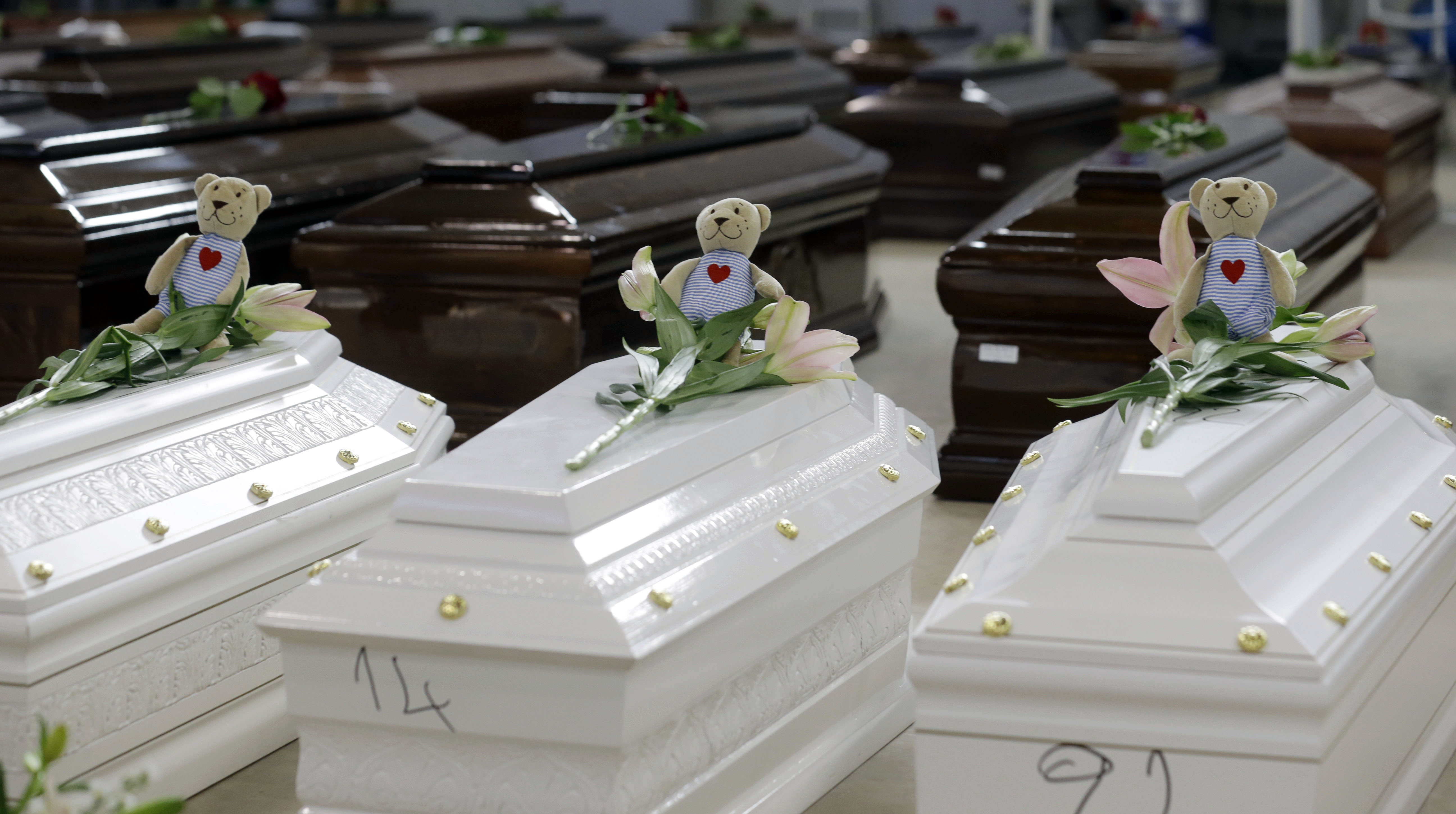 In this Saturday, Oct. 5, 2013 file photo, teddy bears and flowers placed on the coffins of deceased migrants are seen inside a hangar at Lampedusa's airport, Italy, Saturday, Oct. 5, 2013.