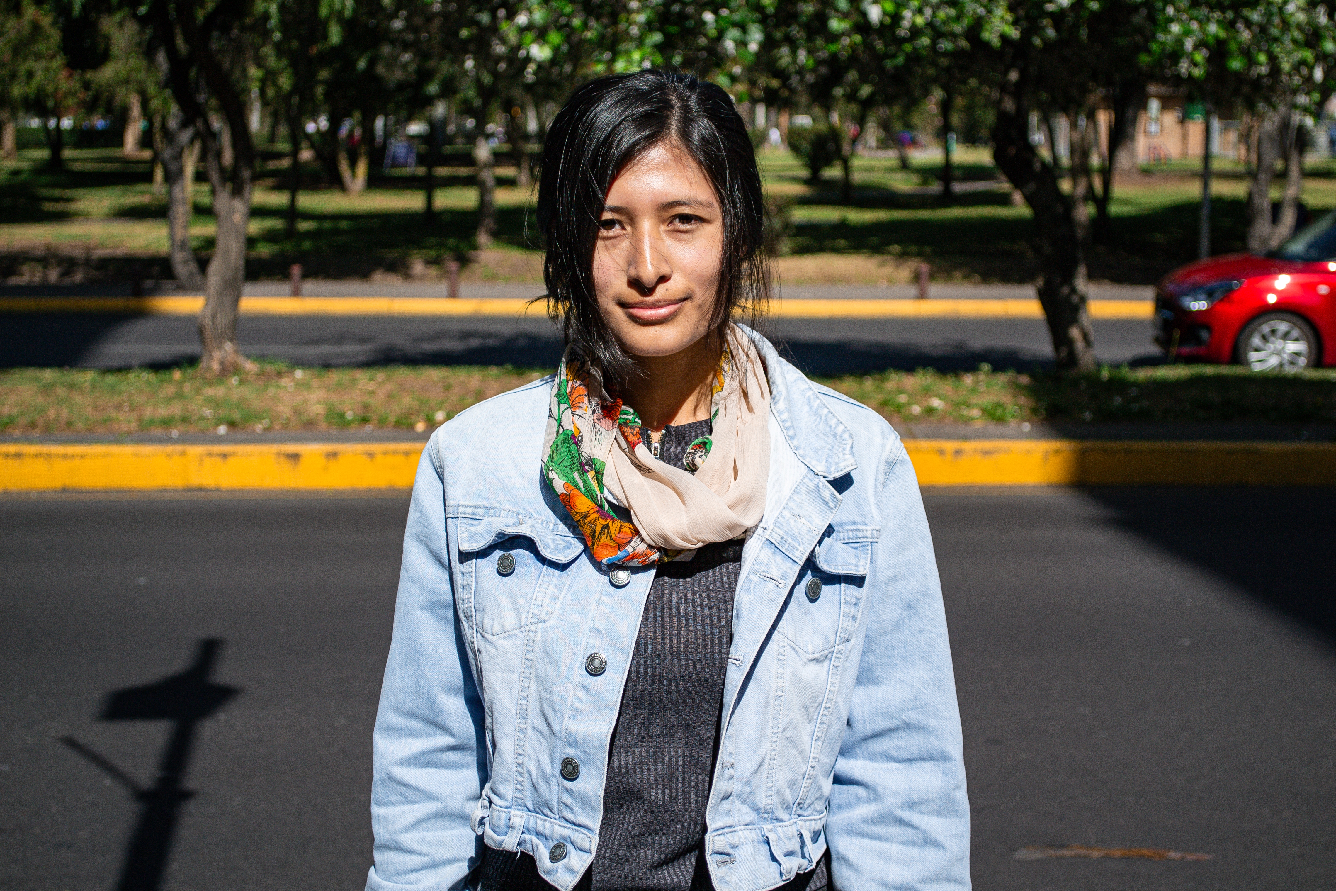 A young woman in a jean jacket stands on a street, facing the camera.