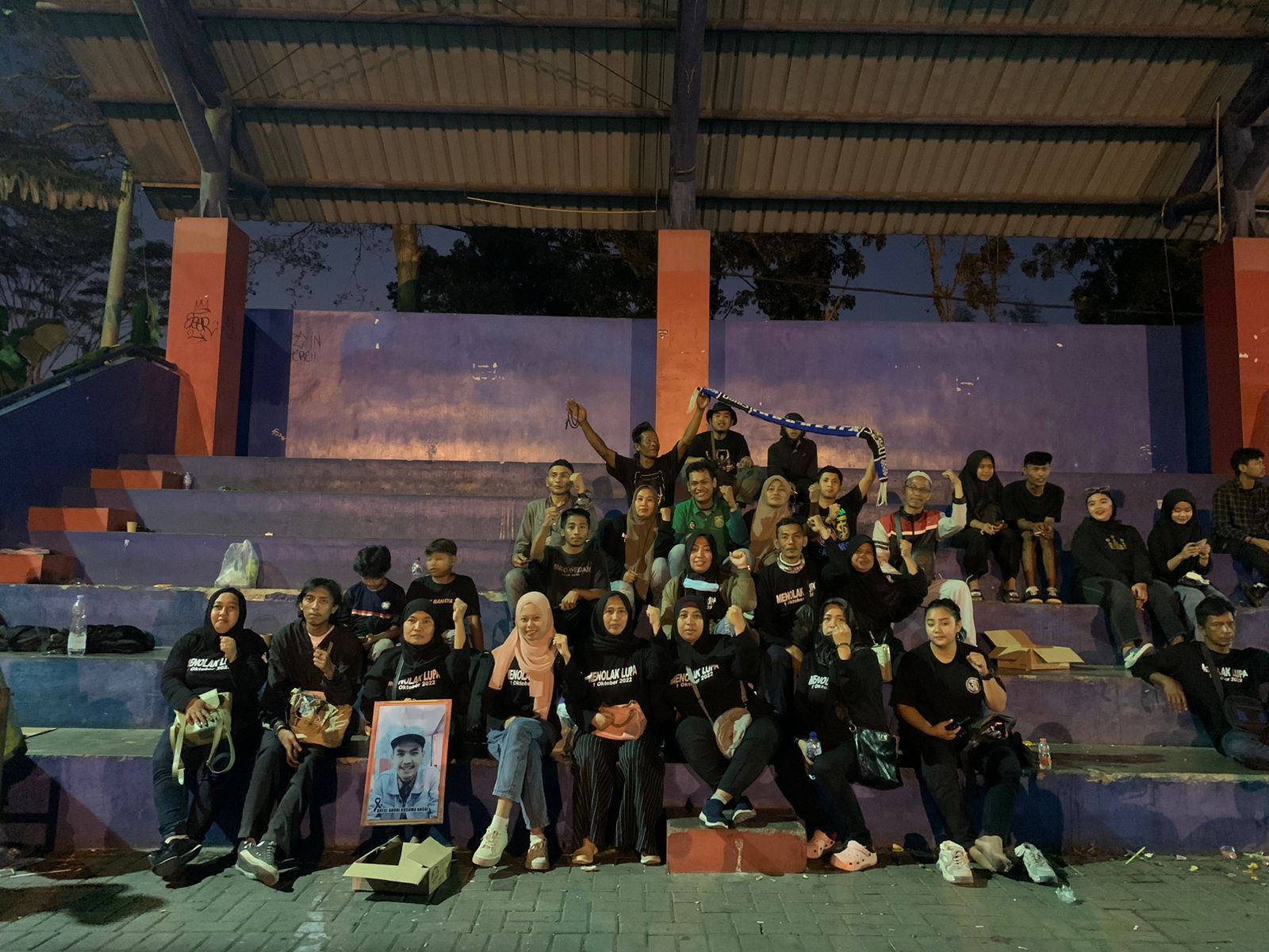 Families sit in their stands as they remember those who died a year ago. They are mostly dressed in black.