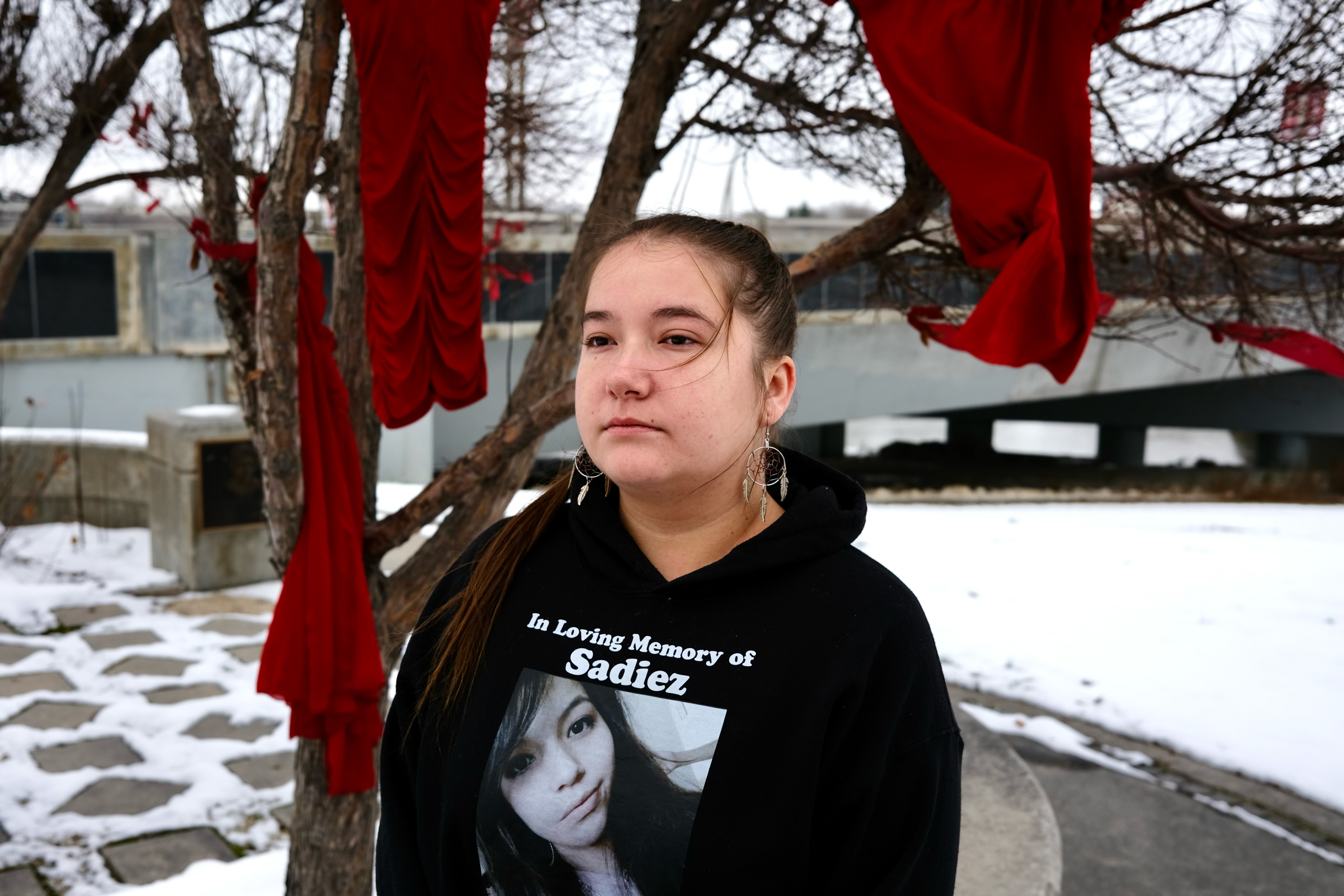 A young woman stands in the snow-covered Manitoba landscape wearing a black hoodie that reads: "In loving memory of Sadiez."