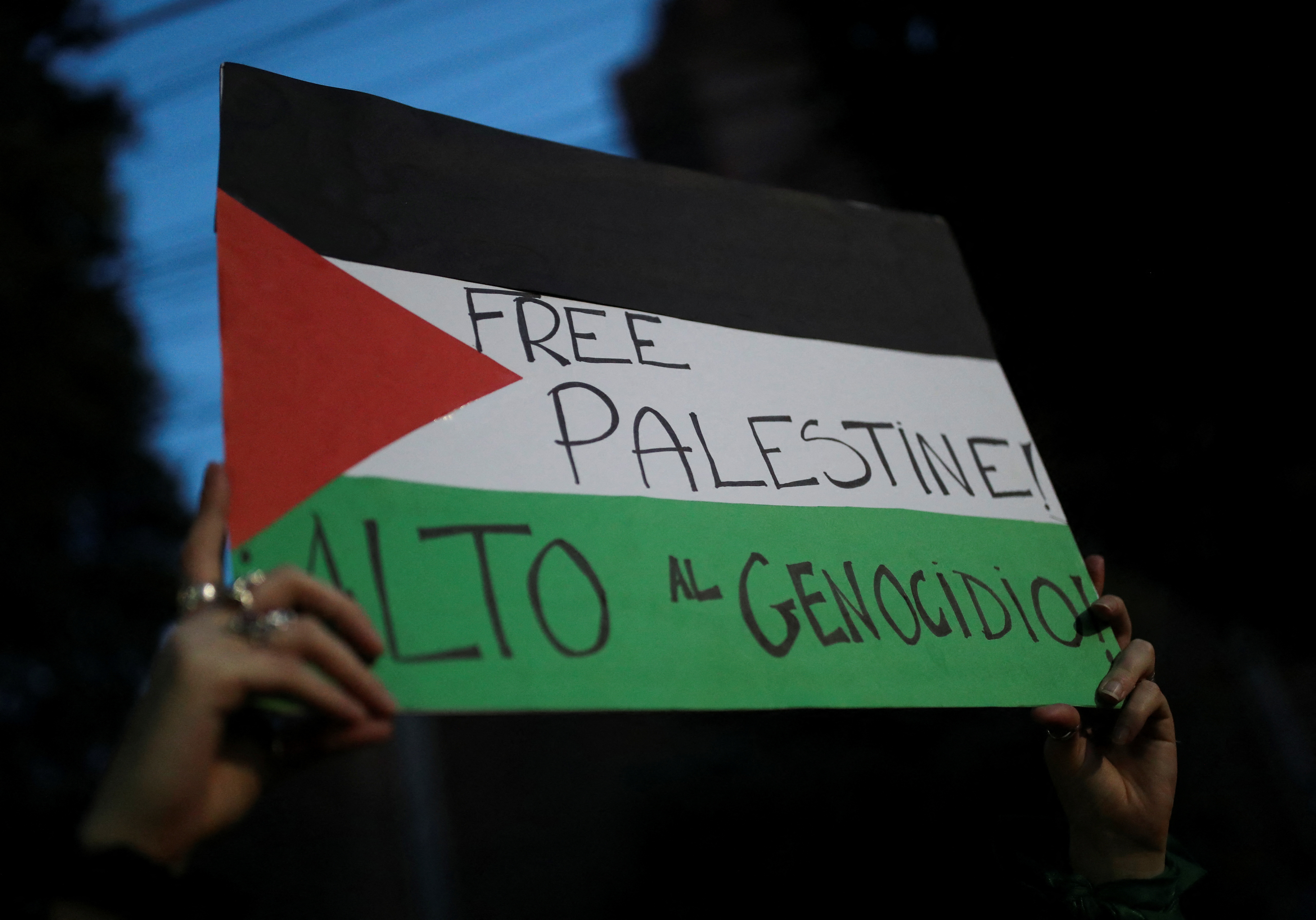 A woman holds a poster that reads "Free Palestine" and "Stop the Genocide" next to other protesters gathered outside the Embassy of Israel during a demonstration in support of the Palestinians, in Mexico City, Mexico