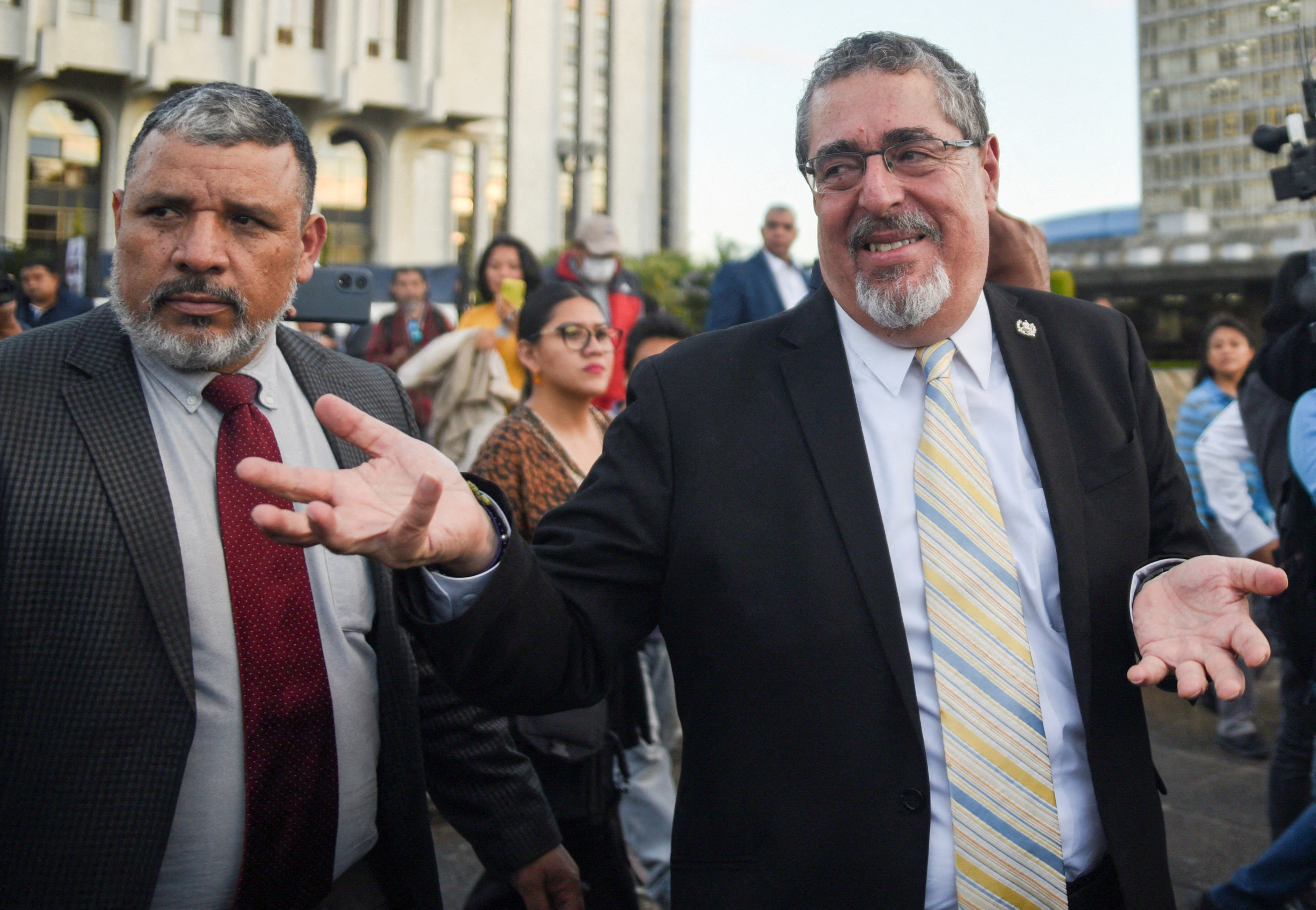 Bernardo Arevalo, dressed in a dark suit and striped tie, gestures in a shrug as he walks outside the Supreme Court in Guatemala City