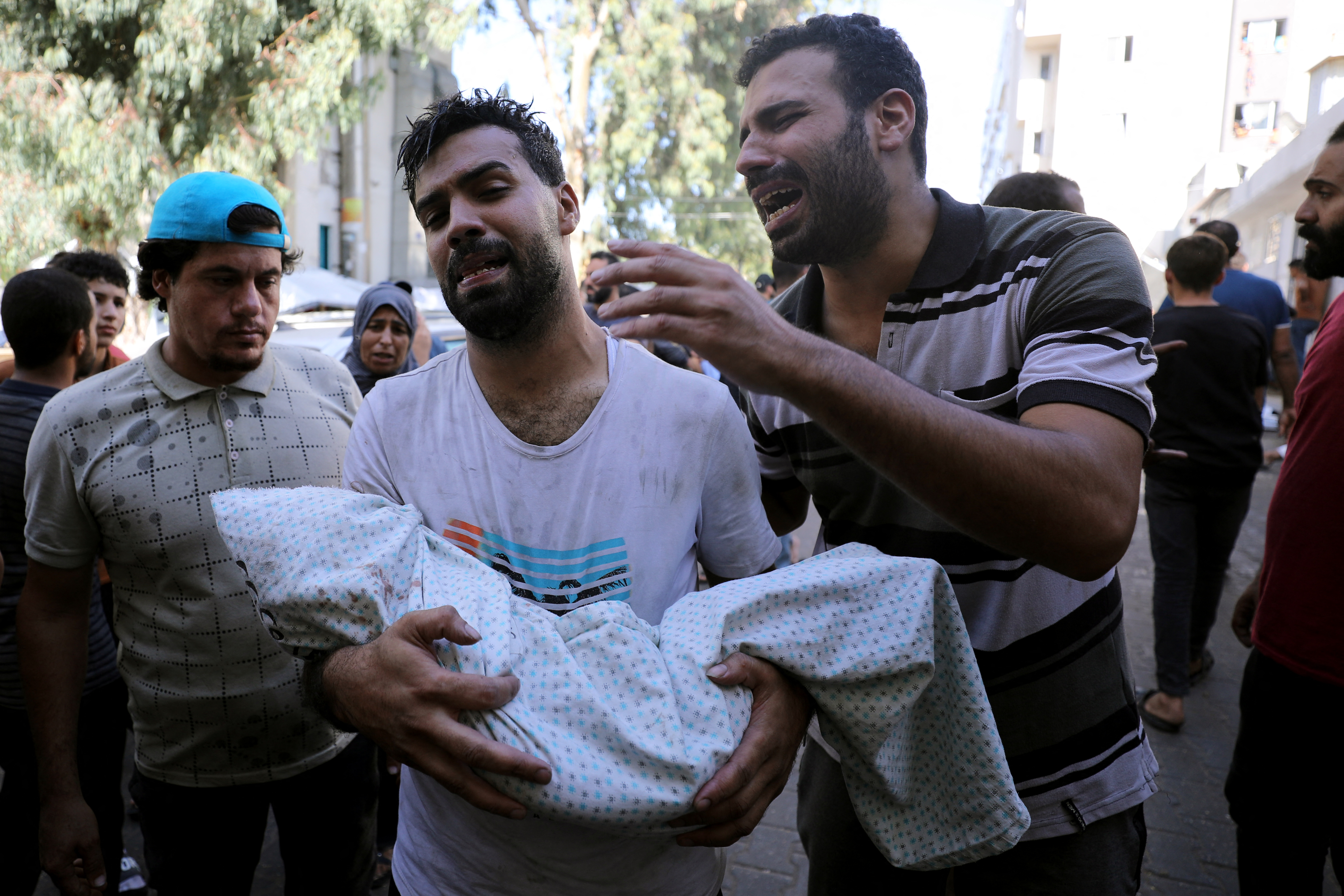 A Palestinian holds the body of a child wrapped in a shroud as another reacts next to him, outside a hospital following Israel's bombardment of Gaza City's eastern suburb of Shujaiya on November 4