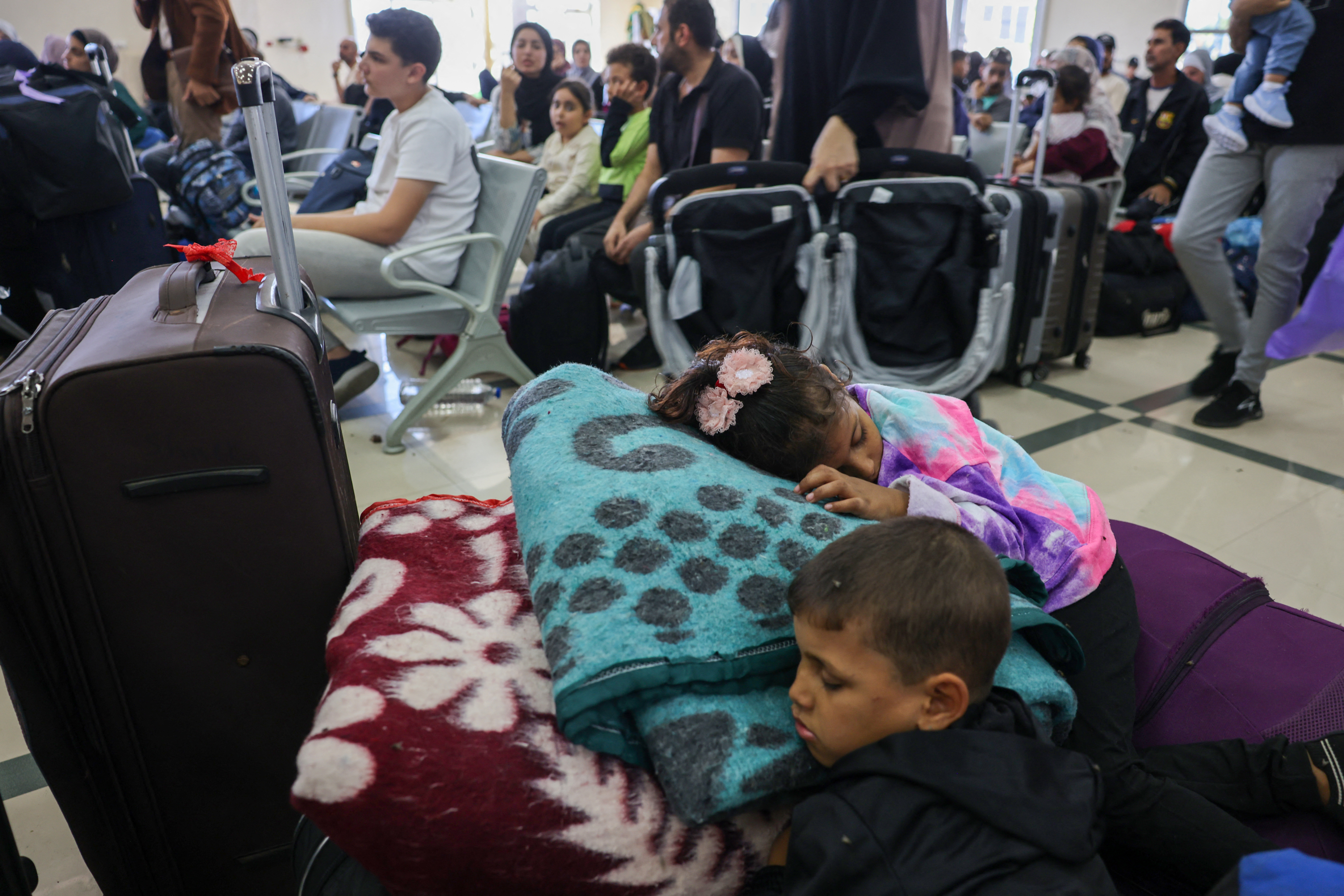 Children sleep as Palestinian dual nationals and foreigners wait to cross the Rafah border crossing with Egypt, in the southern Gaza Strip