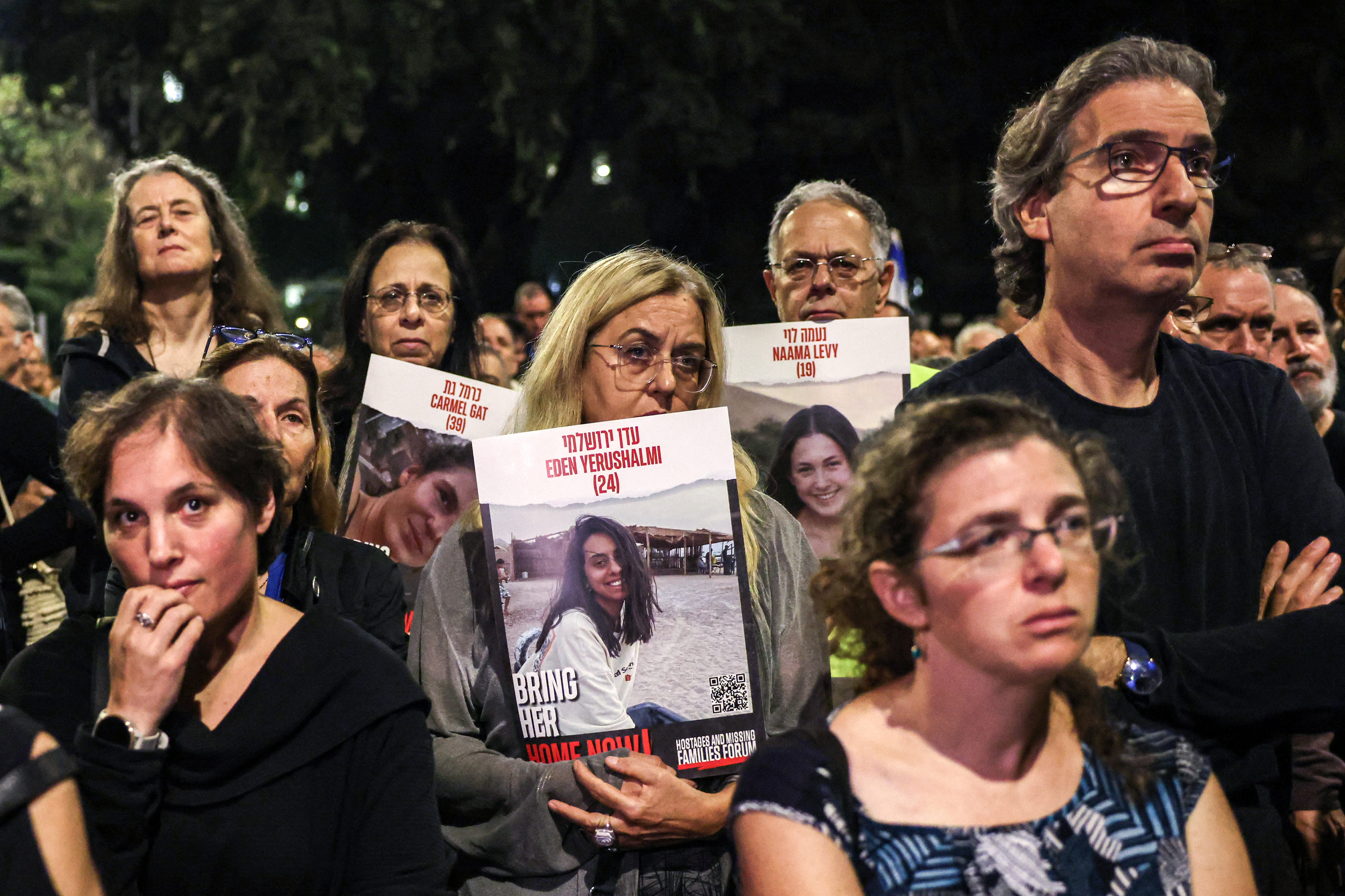 a crowd of people with sad expressions on their face with one holding a sign with a photograph of a young woman saying bring her home now
