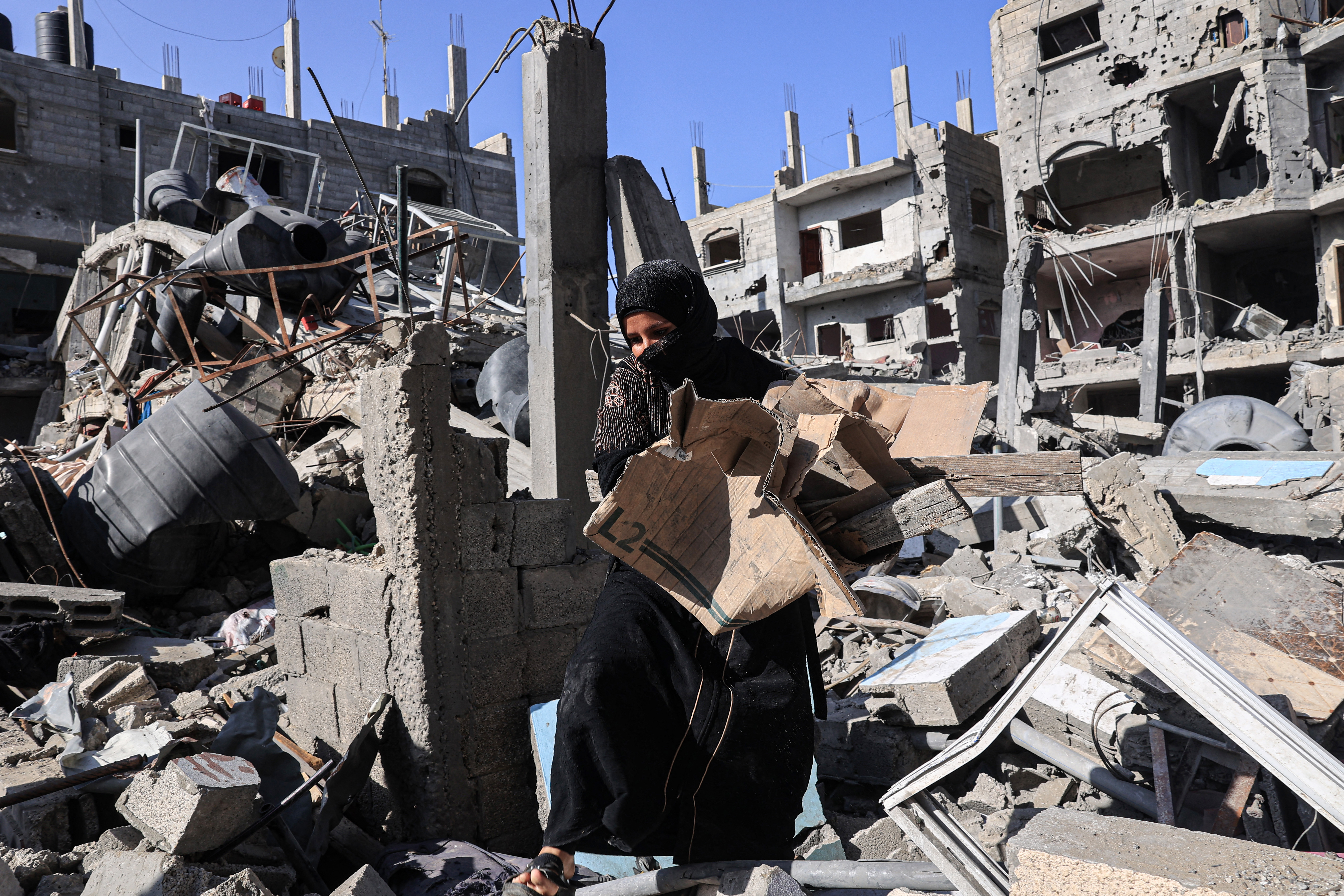 Amal al-Robayaa caries cardboard found amid the rubble of a building destroyed in Israeli bombing, to light a fire for making bread