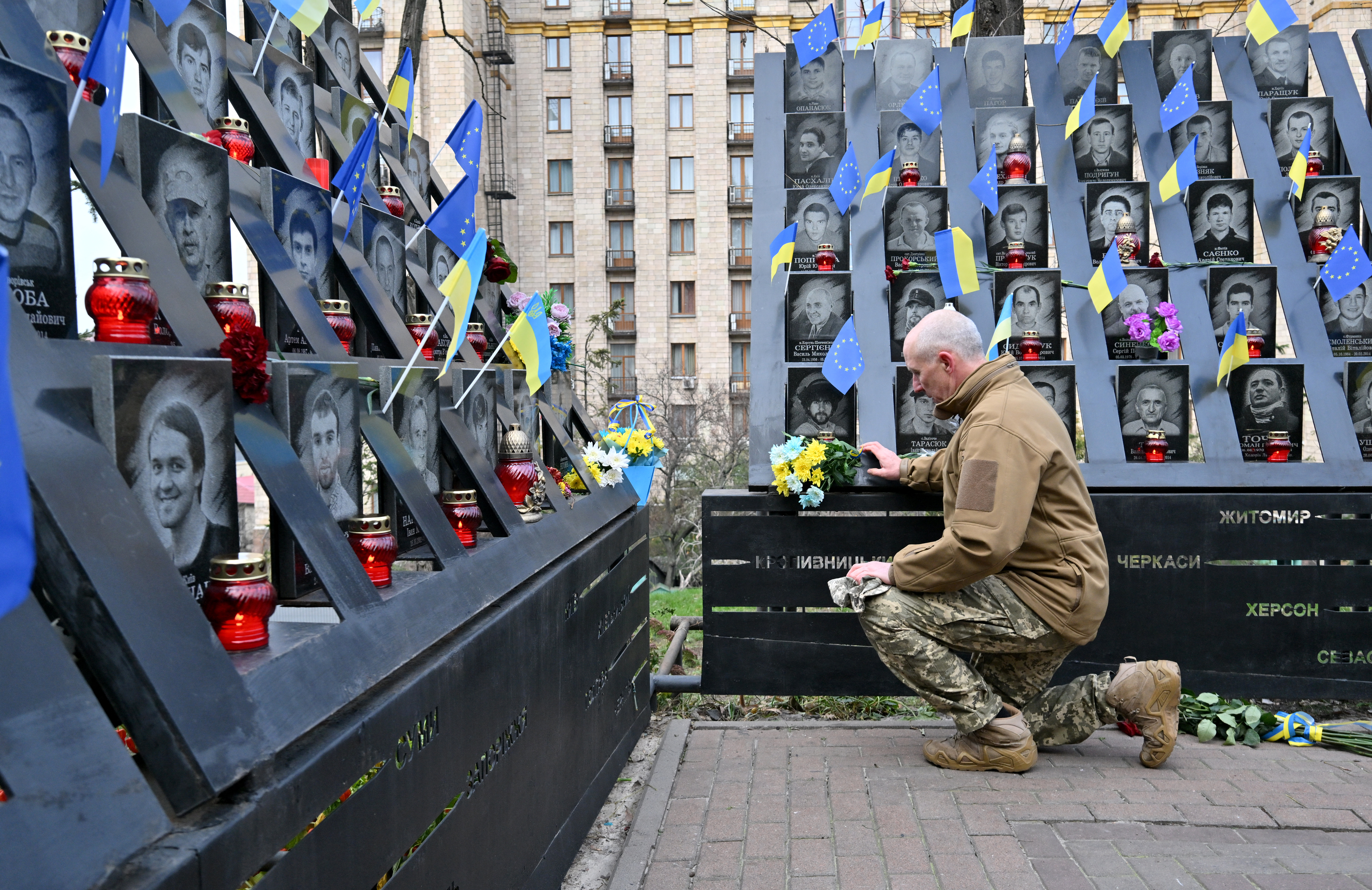 A man in military fatigues kneeling at a memorial to those who died in the Maidan between 2013-2014