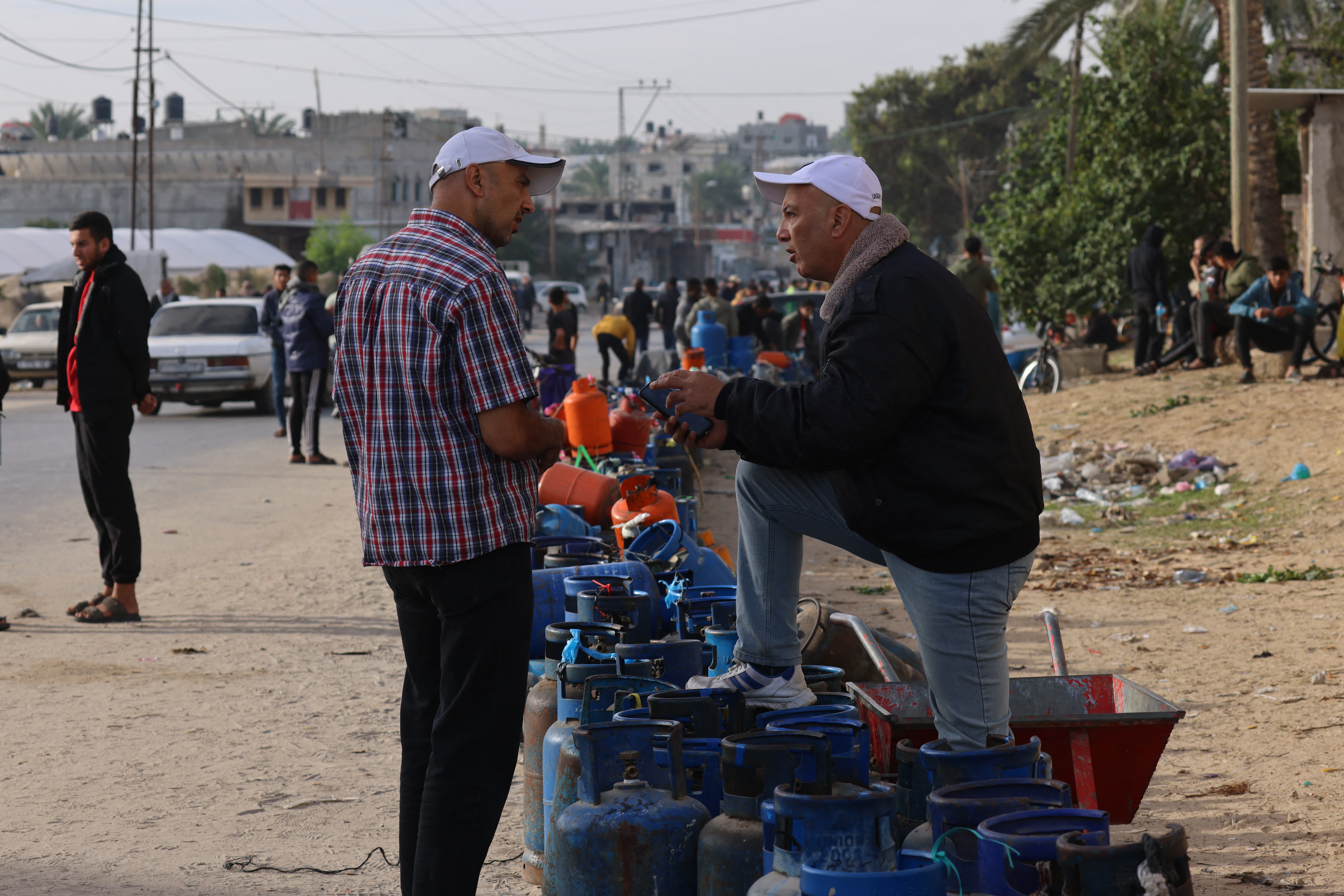 People wait near empty gas canisters to be filled with cooking gas from a tank that entered the Palestinian enclave via the Rafah crossing with Egypt, in Rafah in the southern Gaza Strip on November 25