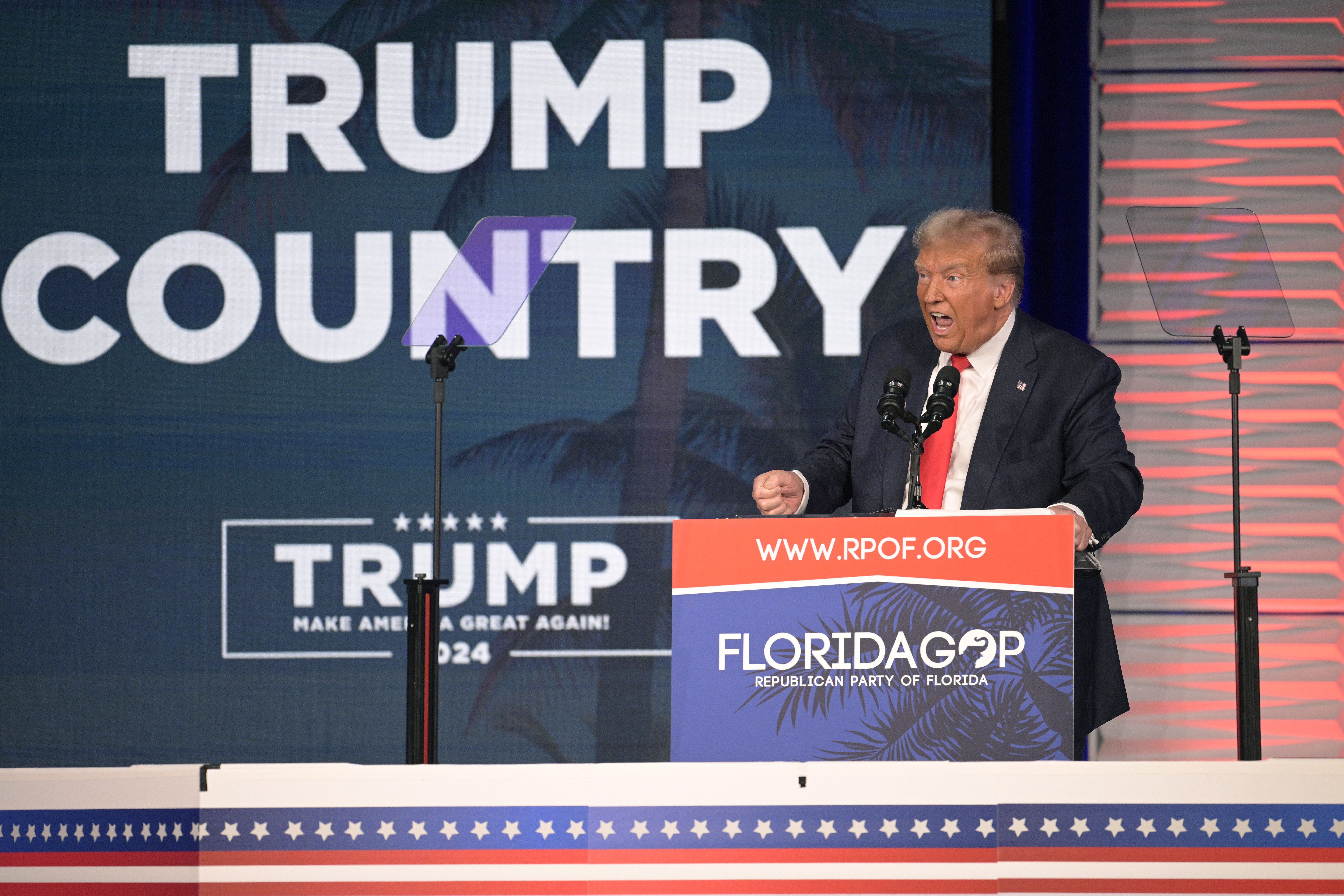 Donald Trump stands behind a Florida GOP podium, speaking to an audience. Behind him is a sign that reads, "Trump Country."