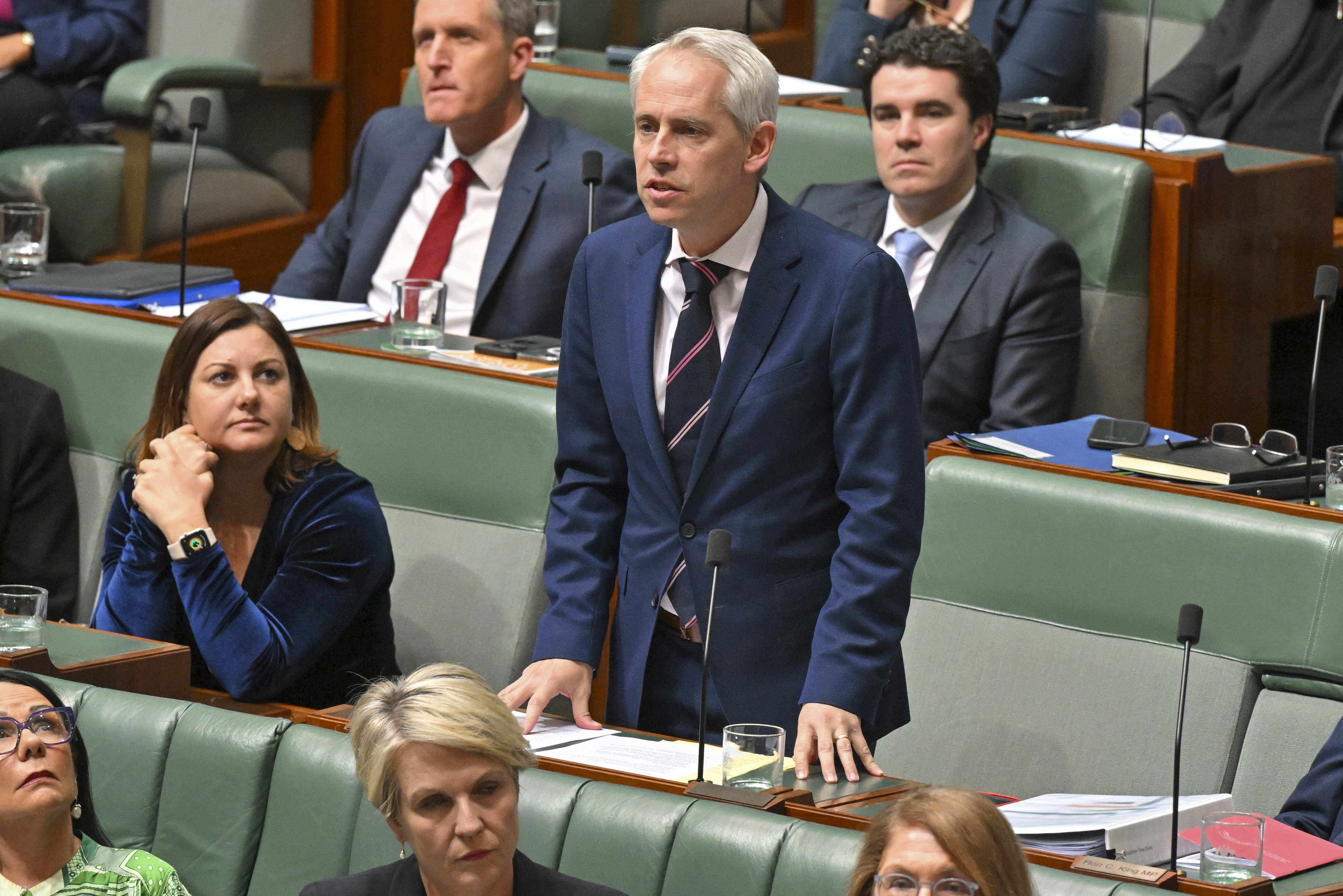 Minister for Immigration Andrew Giles speaking in Australia's parliament. He is standing. Other MPs ate on the benches around him.