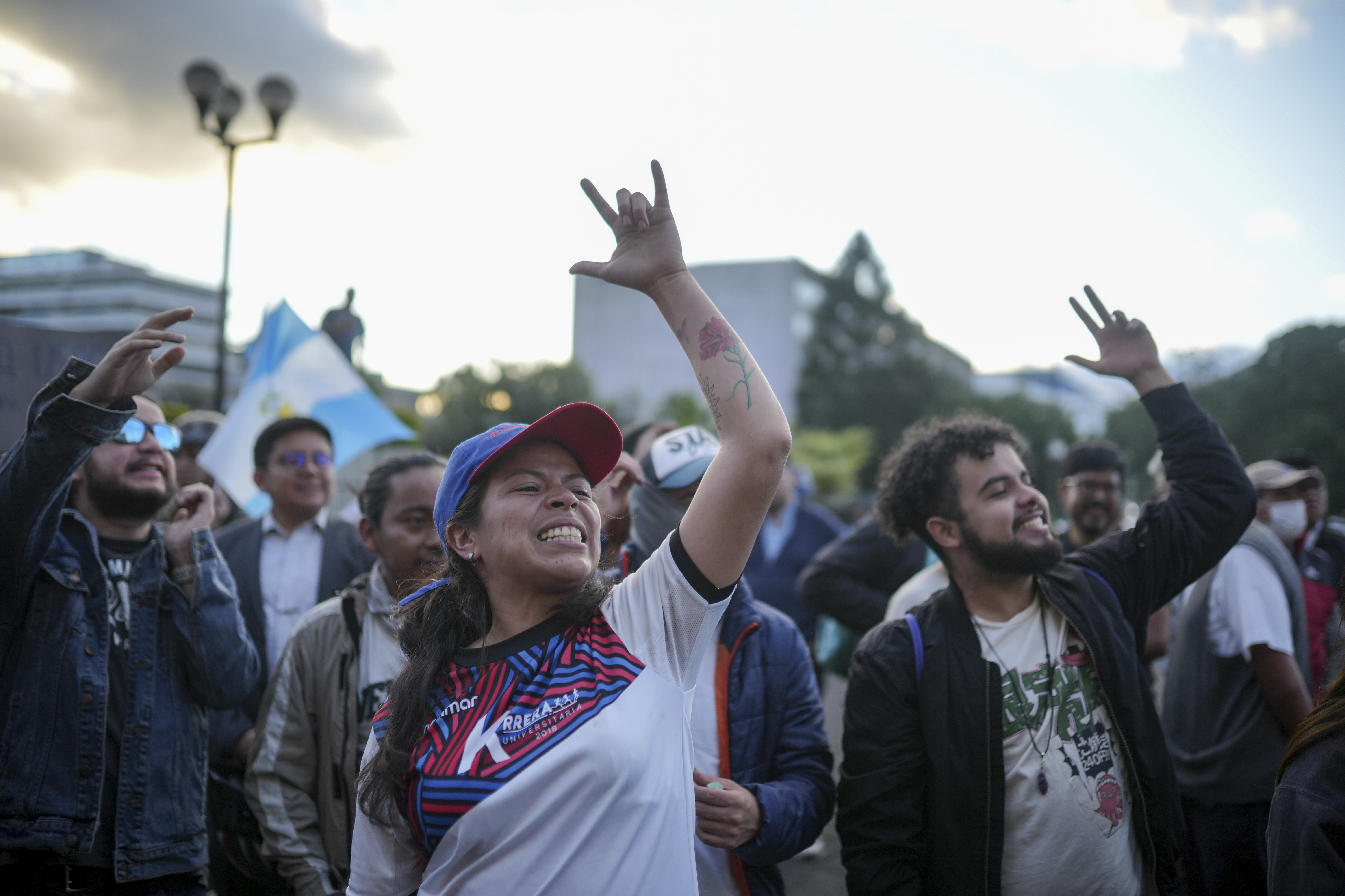 A protester in a baseball cap makes the sign language symbol for love with her raised hand as she joins others on the street in support of Bernardo Arevalo.