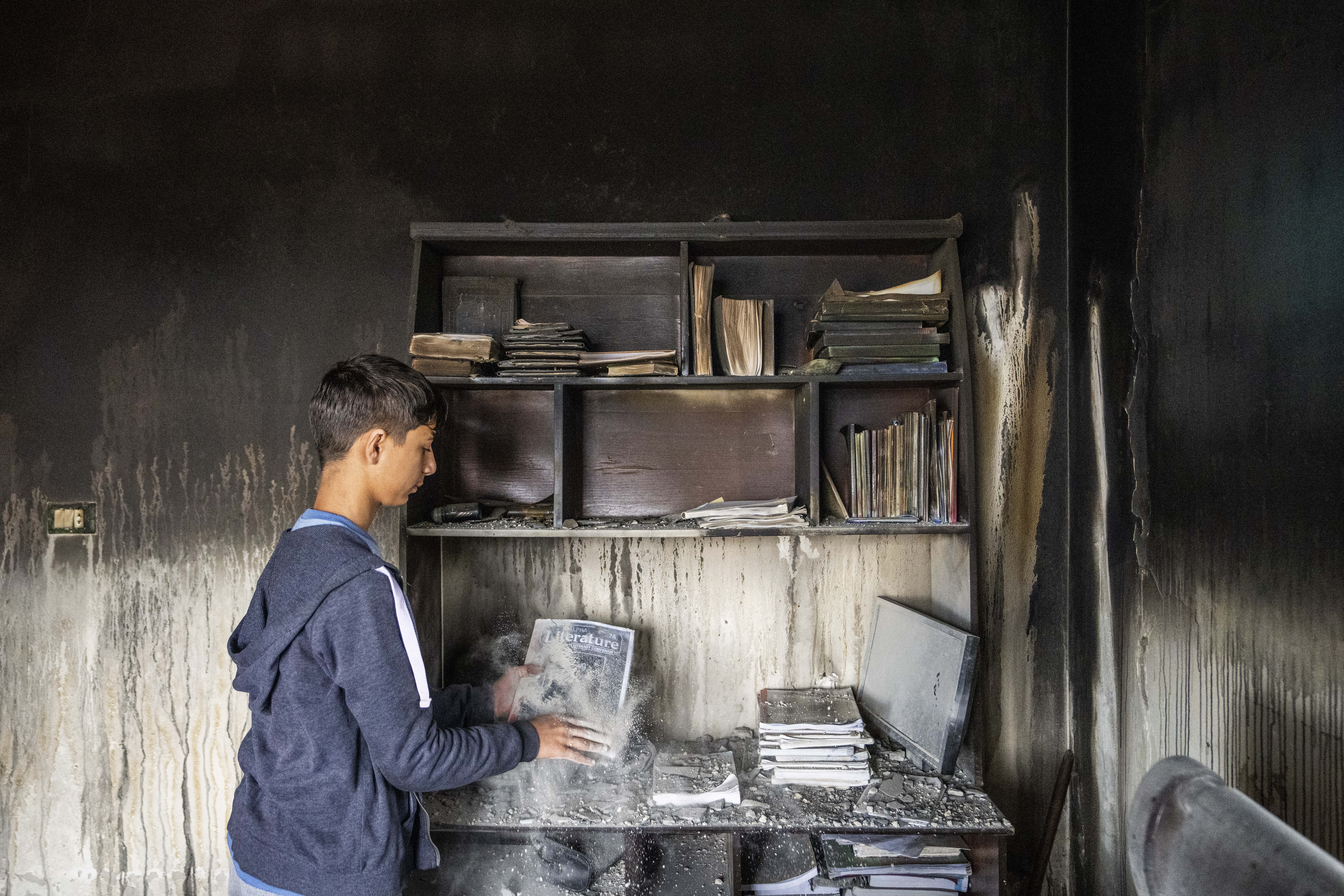 Ali Fawaz checks destroyed books and notebooks inside his damaged family house that was hit by Israeli shelling in the Kfar Kila border village with Israel in south Lebanon.