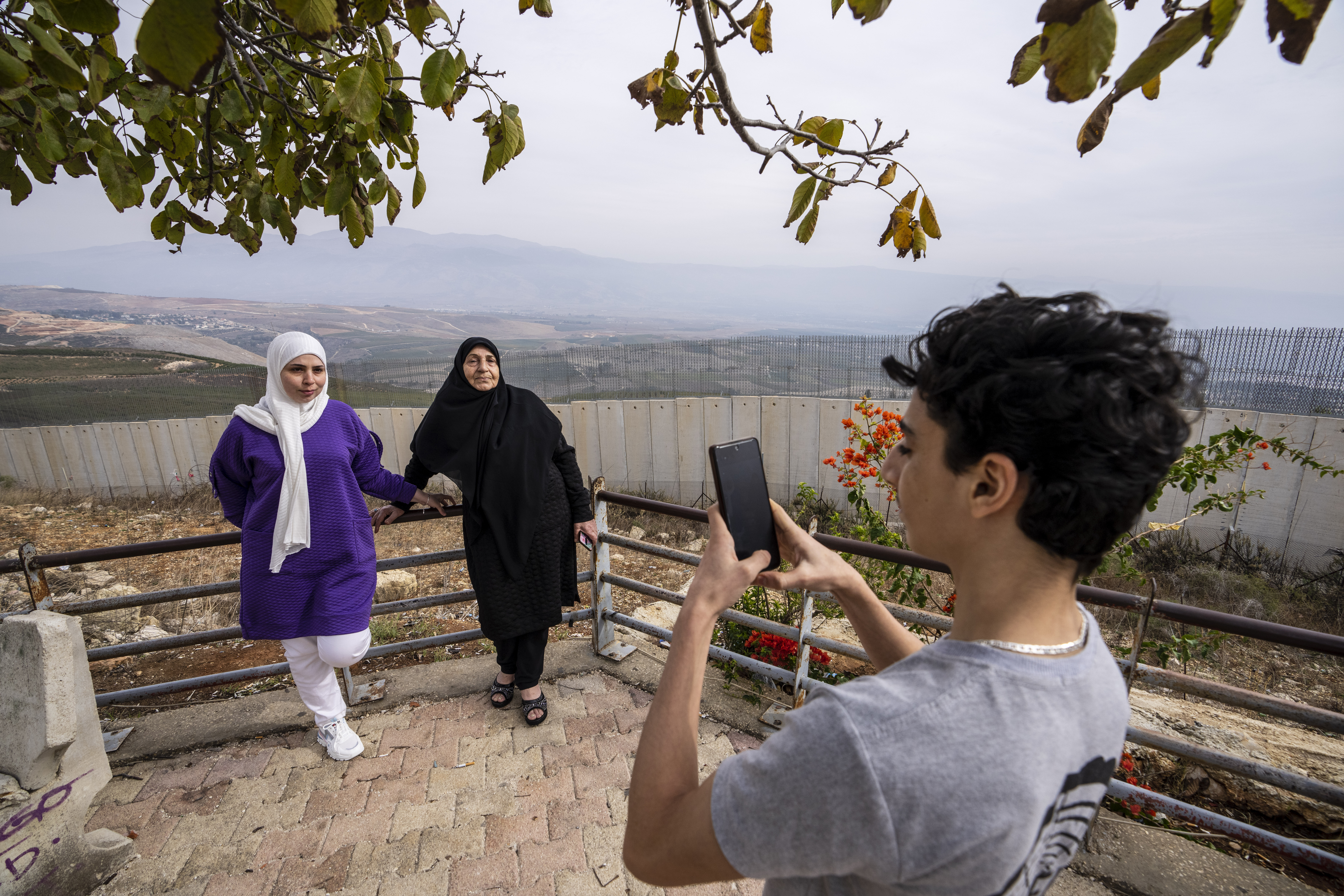 A boy takes a souvenir picture on his mobile phone to his family in front of a wall that build by Israel, background, in Odaisseh border village with Israel, south Lebanon.