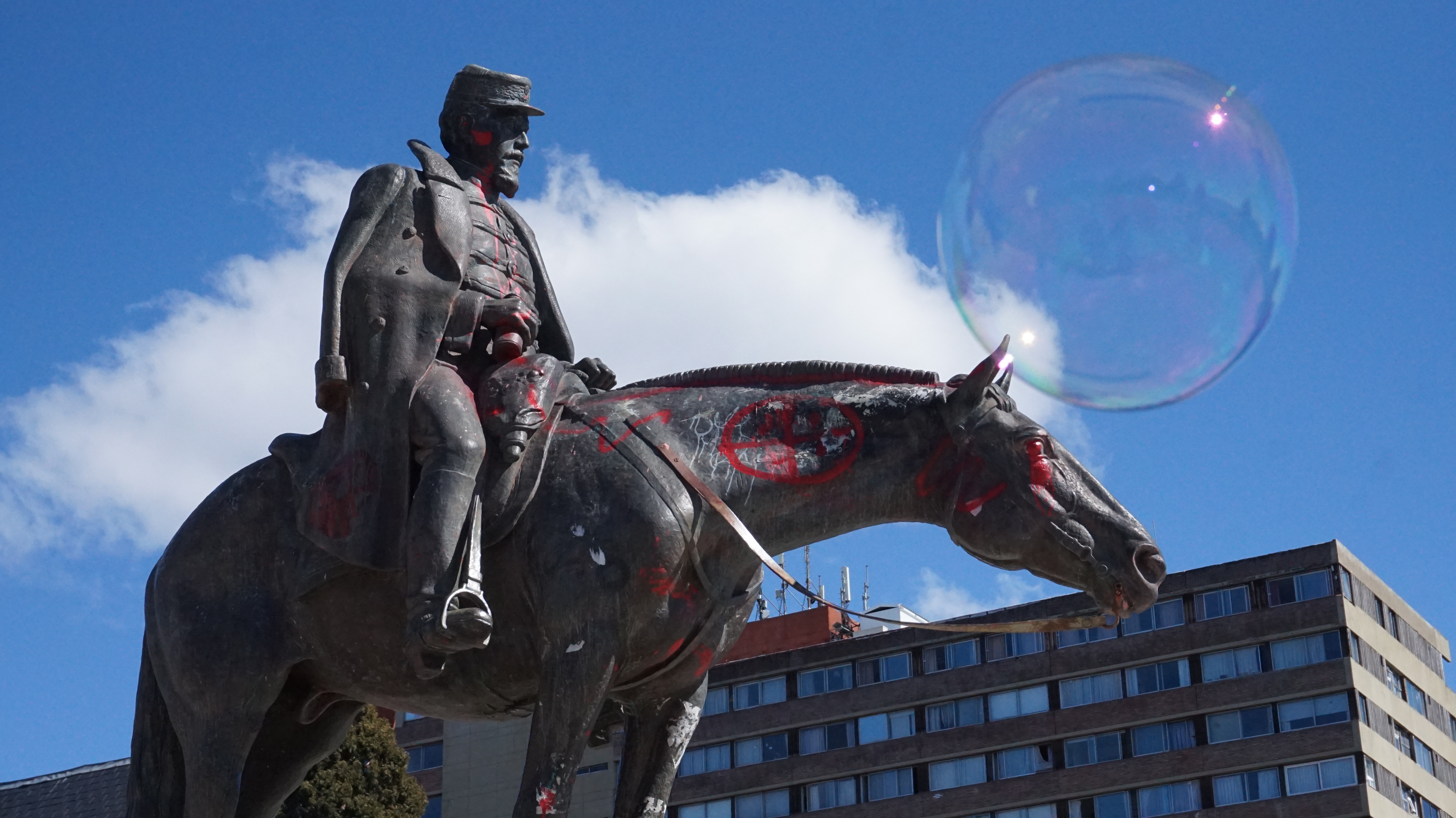 A bronze statue of a soldier atop a horse is covered in red graffiti.