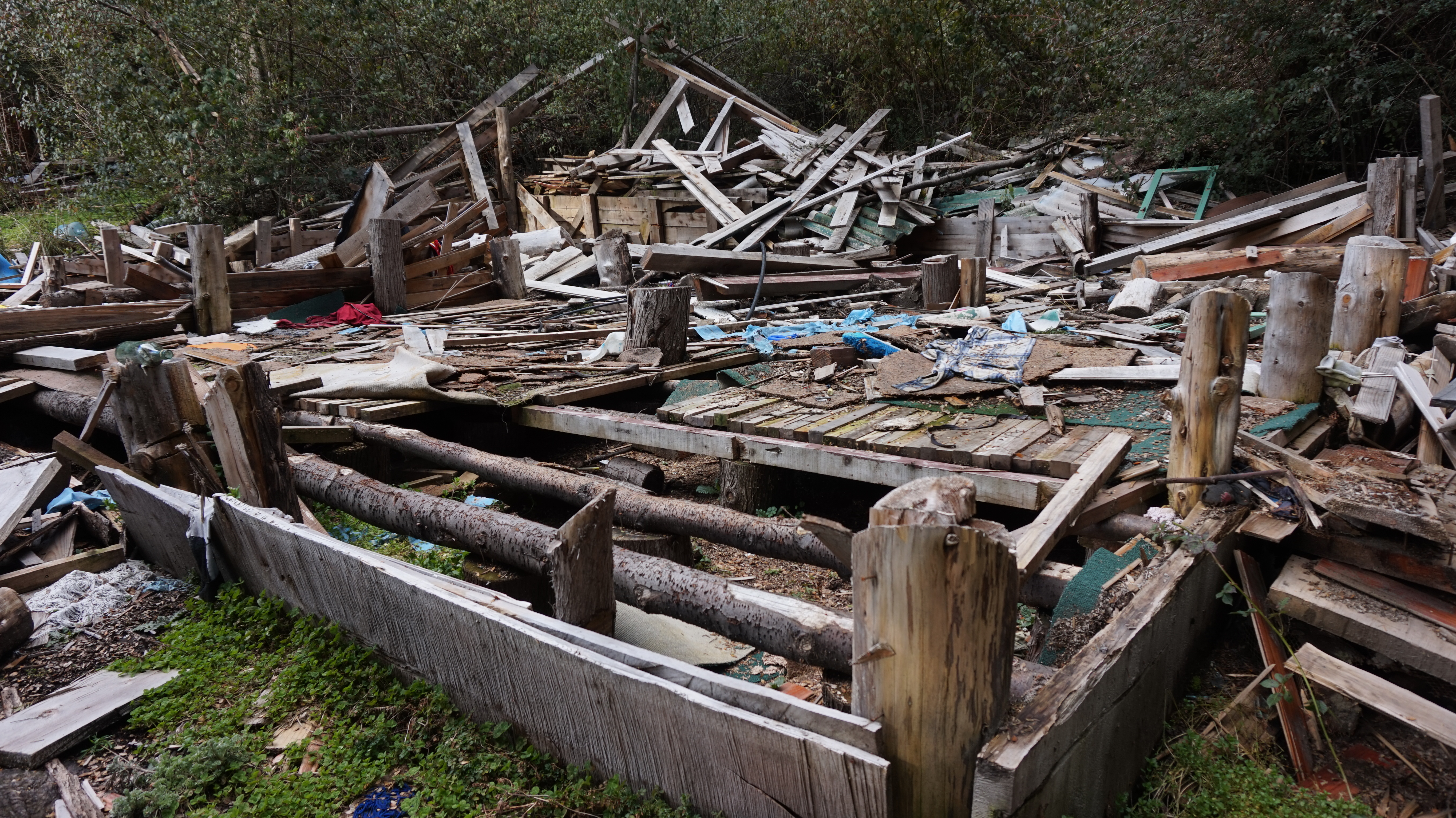 A wooden house lies in ruins, its outline still visible below the rubble.