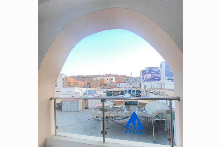 A photo of a view from a window with a makeshift bed on a roof and houses in the distance.