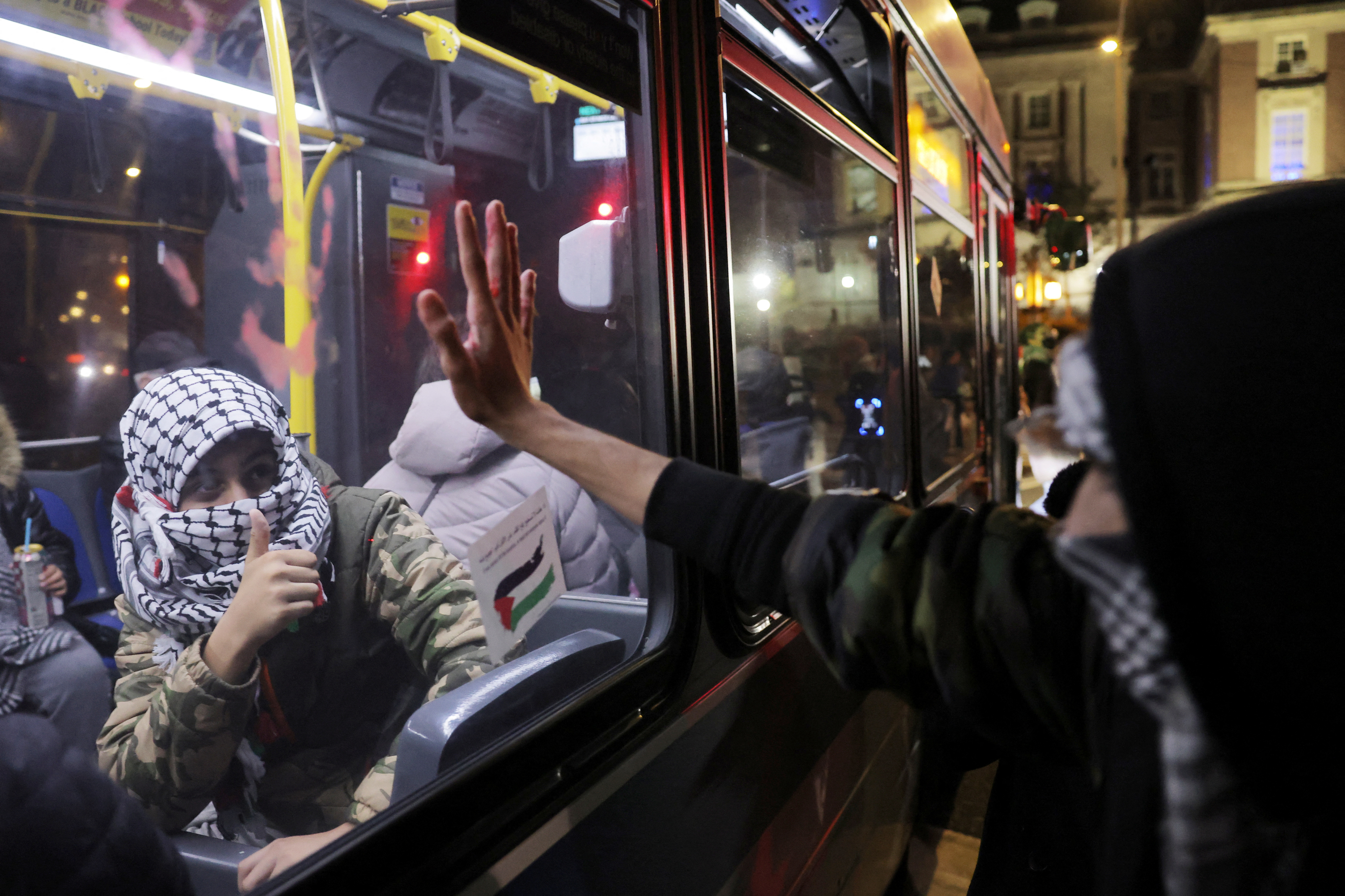 A person in a keffiyeh gestures in support of another protestor outside of the window