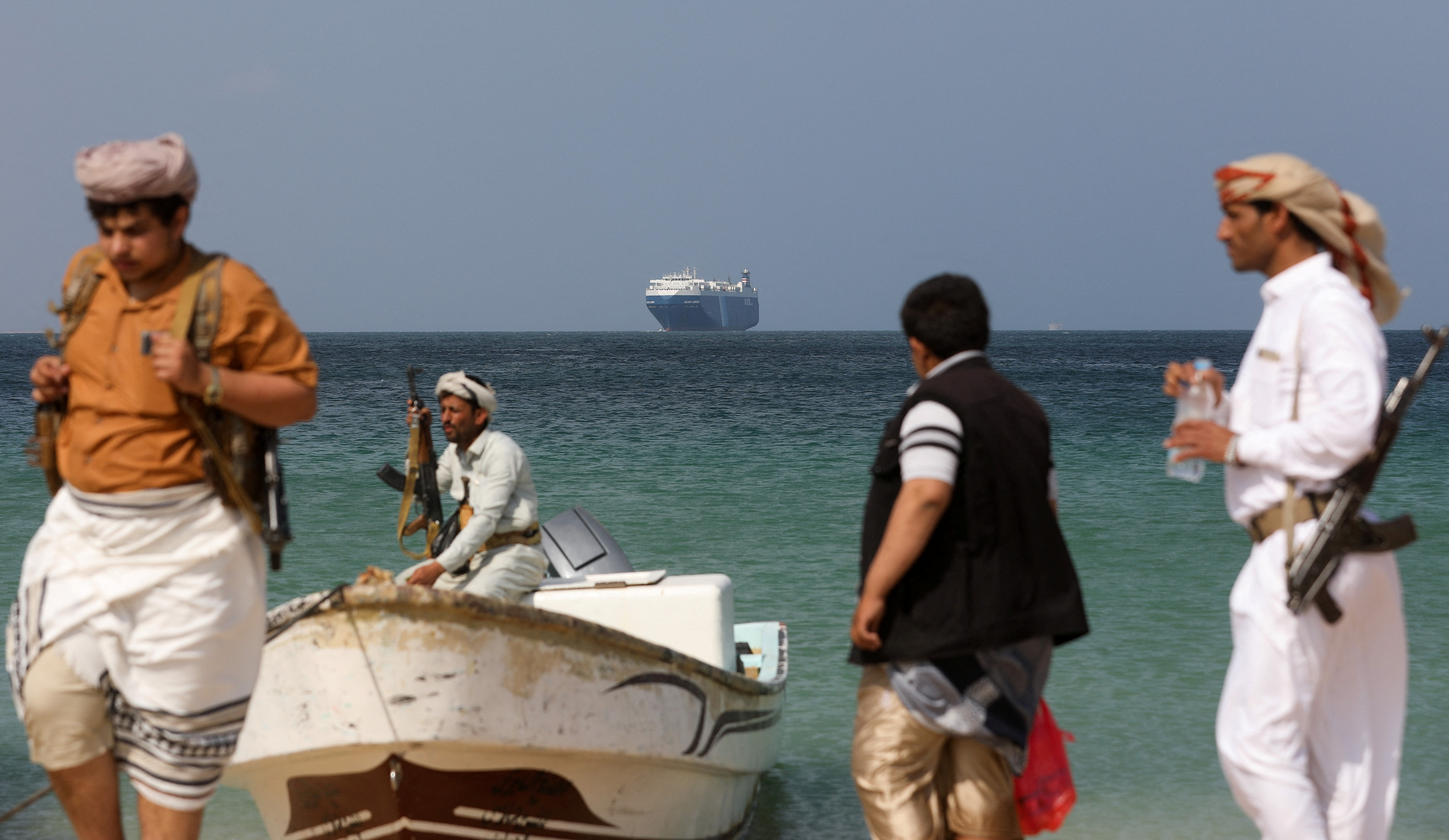 Armed men stand on the beach as the Galaxy Leader commercial ship, seized by Yemen's Houthis last month, is anchored off the coast of al-Salif, Yemen, on December 5, 2023 [Khaled Abdullah/Reuters]