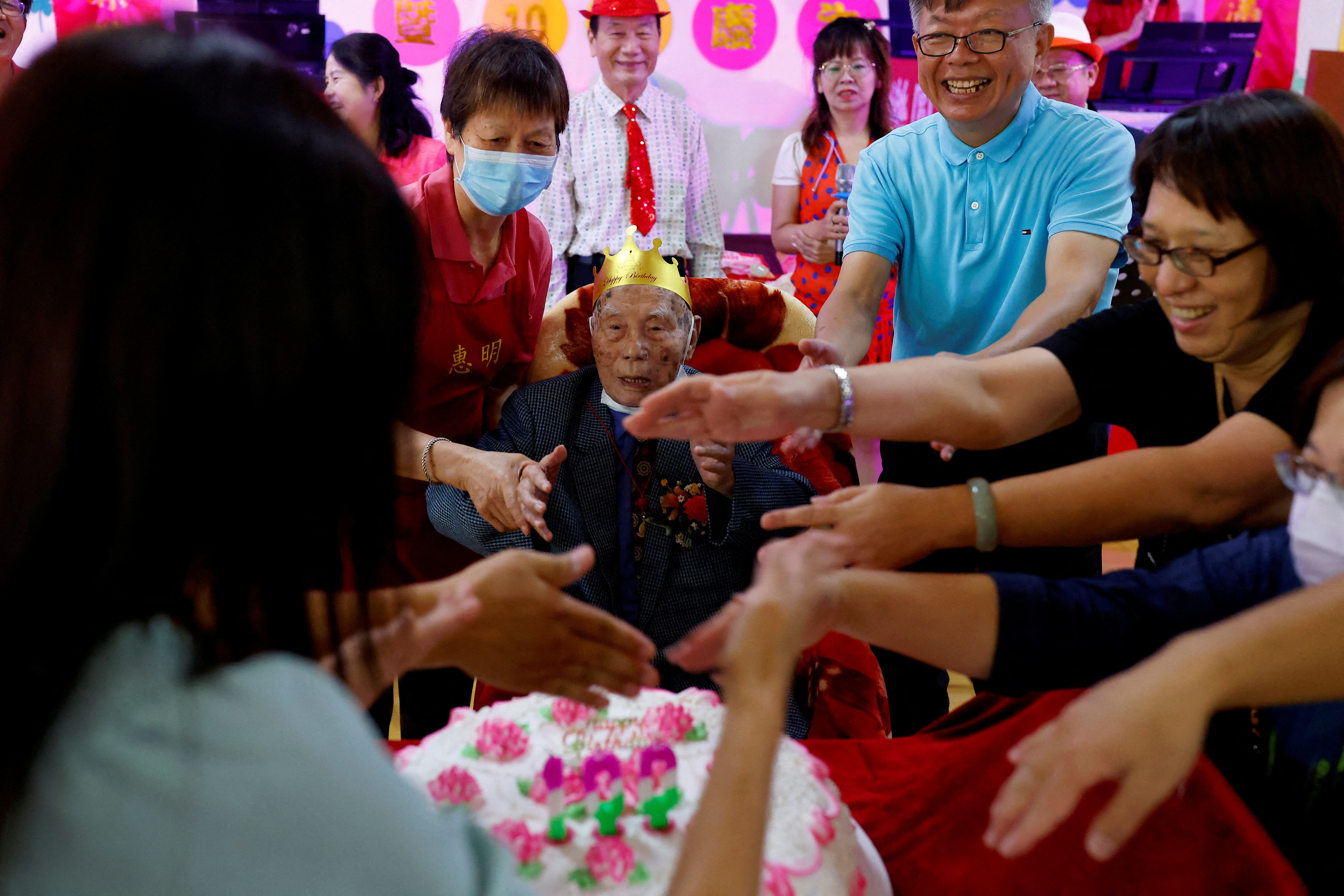 Shi Kuo-yu, a resident of the Taoyuan Veterans Home who is turning 100 years old, waves at the candles of his cake with the home's staff during the birthday celebration in Taoyuan, Taiwan.