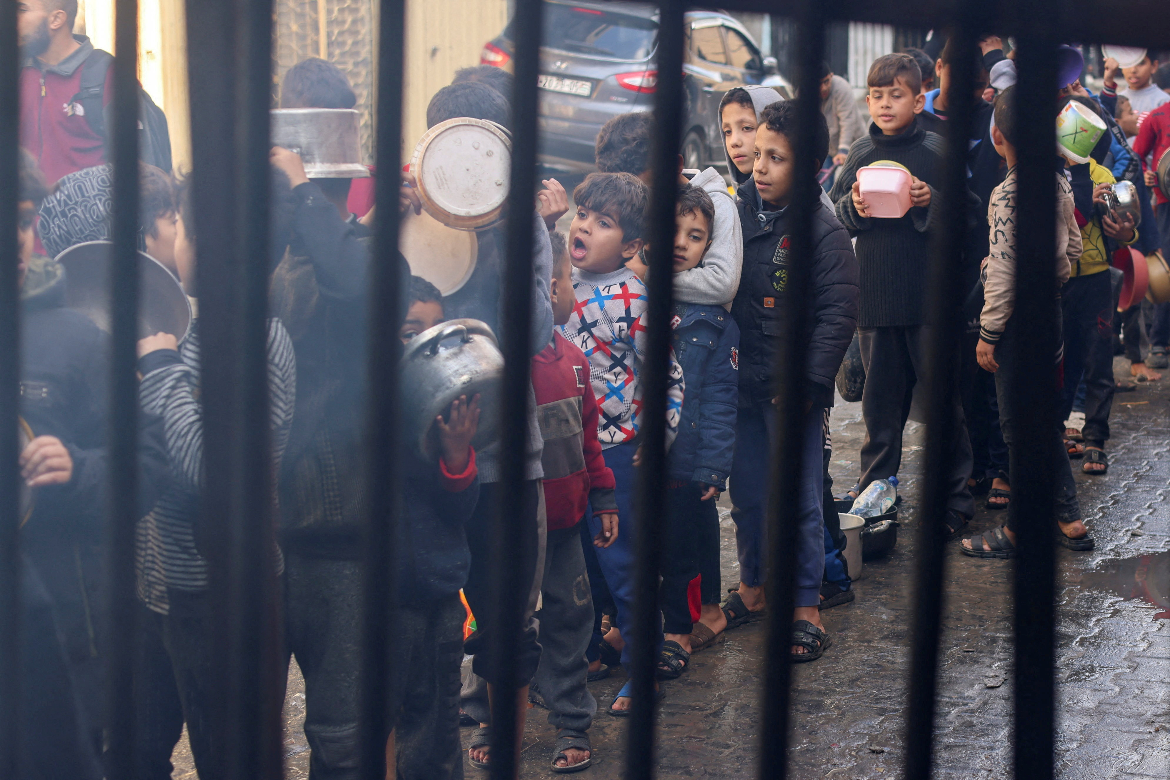 Palestinian children carry pots as they queue to receive food cooked by a charity kitchen, amid shortages in food supplies, as the conflict between Israel and Hamas continues, in Rafah in the southern Gaza Strip.