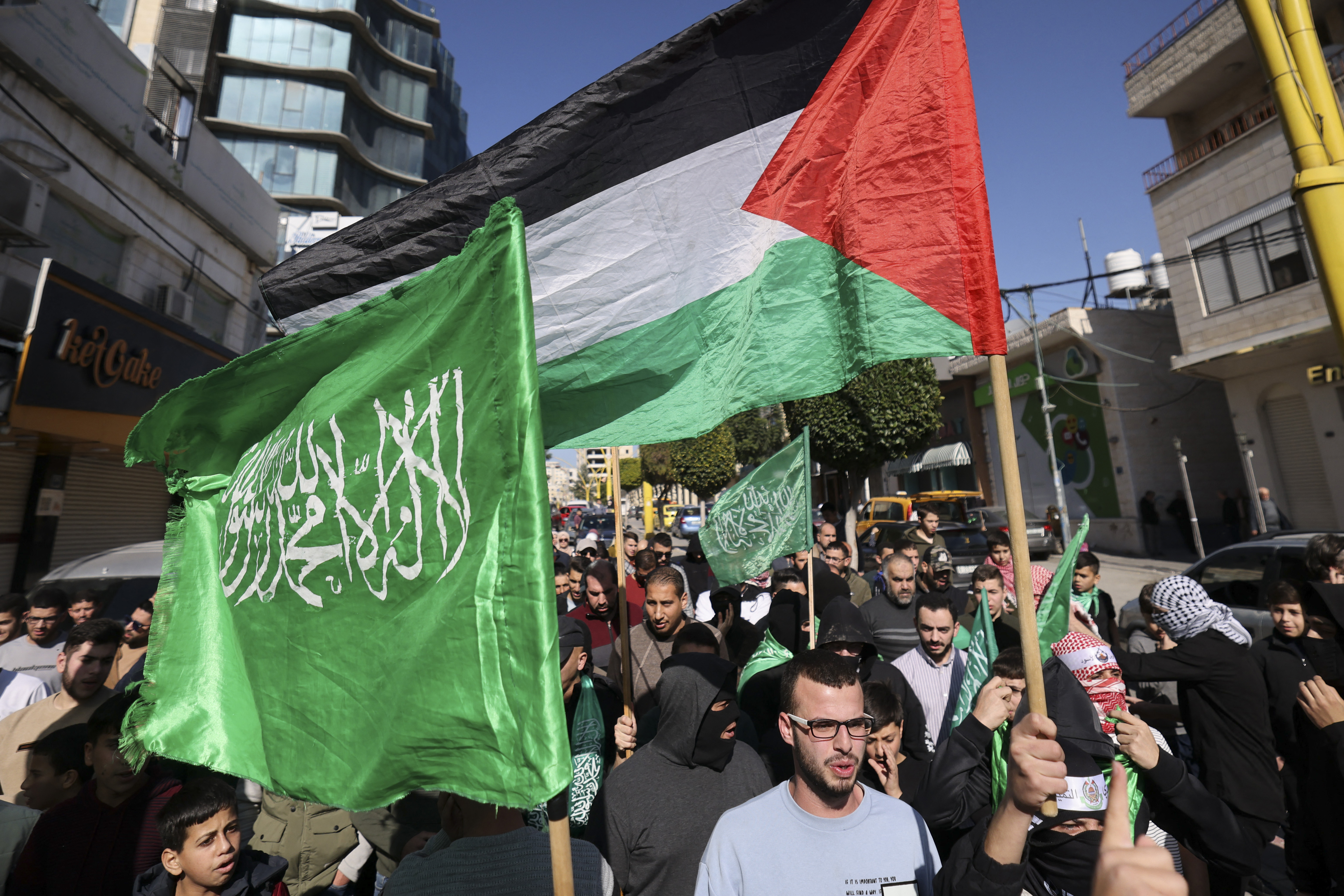 Palestinians raise their national flag as well as flags of the Hamas movement during a rally in the occupied West Bank city of Hebron in support of the Gaza Strip, as battles between Israel and Hamas resumed on December 1, 2023