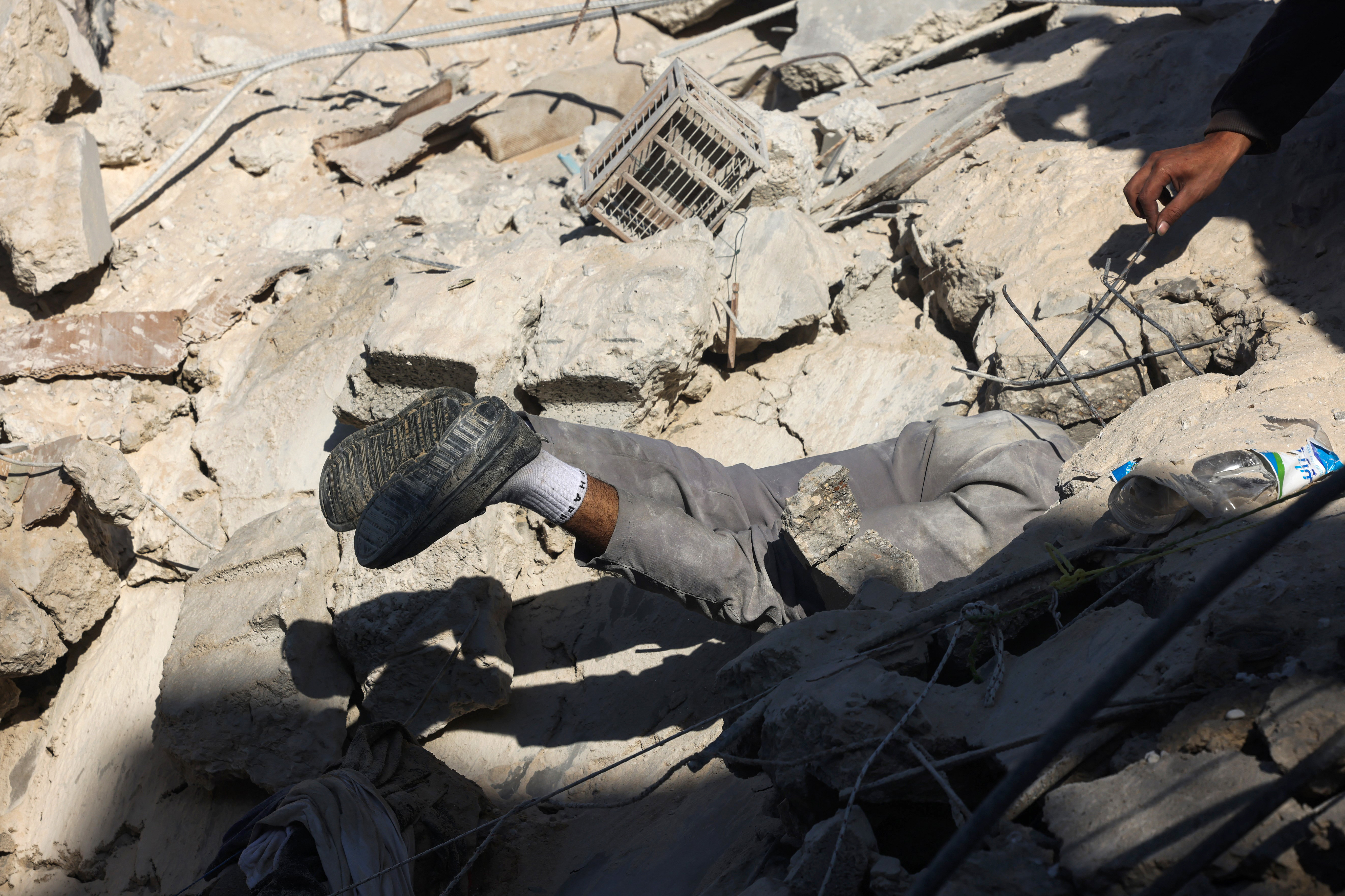 A Palestinian man searches for survivors beneath the rubble of a building following Israeli bombing in Rafah in the southern Gaza Strip on December 3