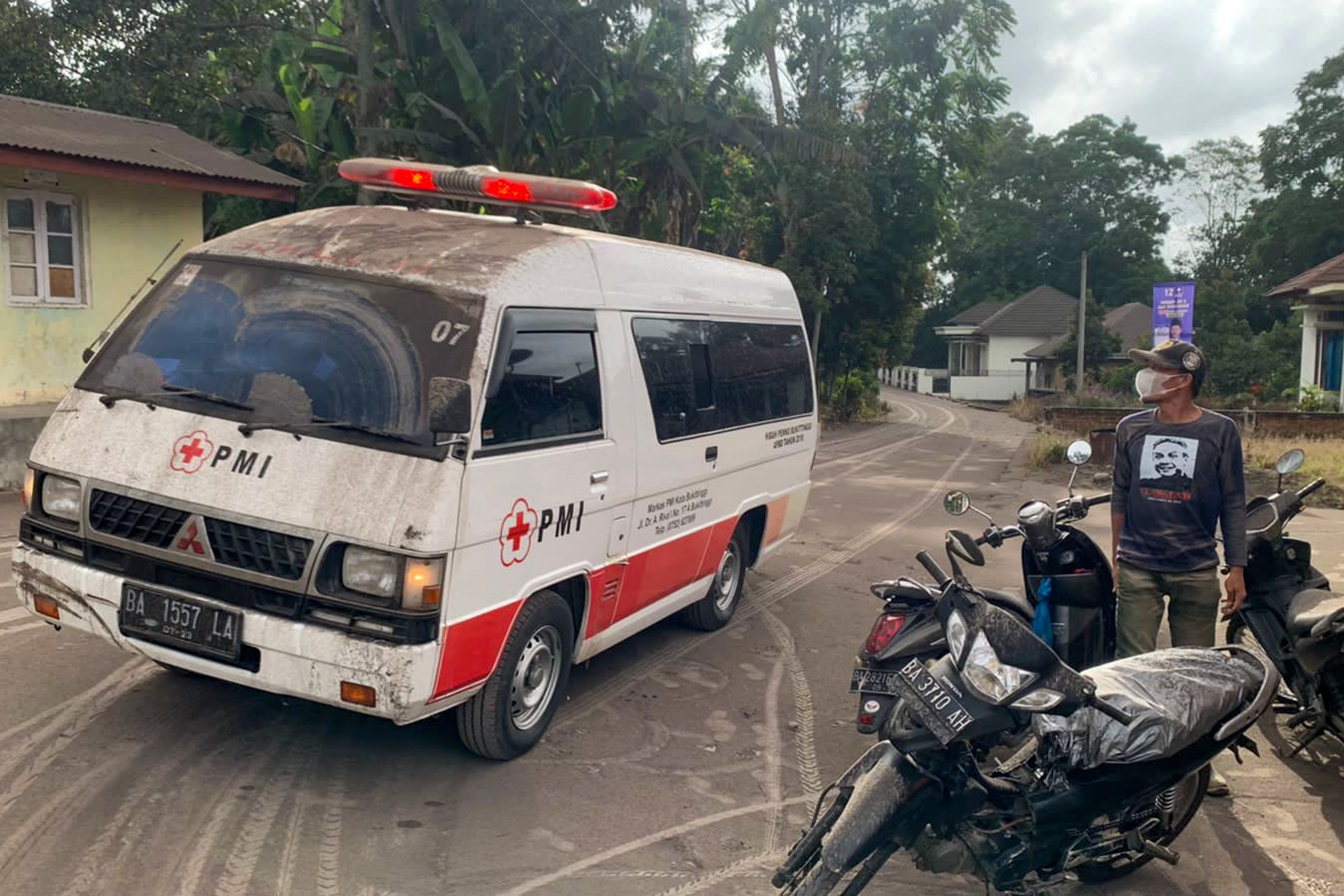 an emergency vehicle driving past as volcanic ash from the eruption of Mount Marapi on Sumatra island covers the village of Nagari Lasi in Agam Regency