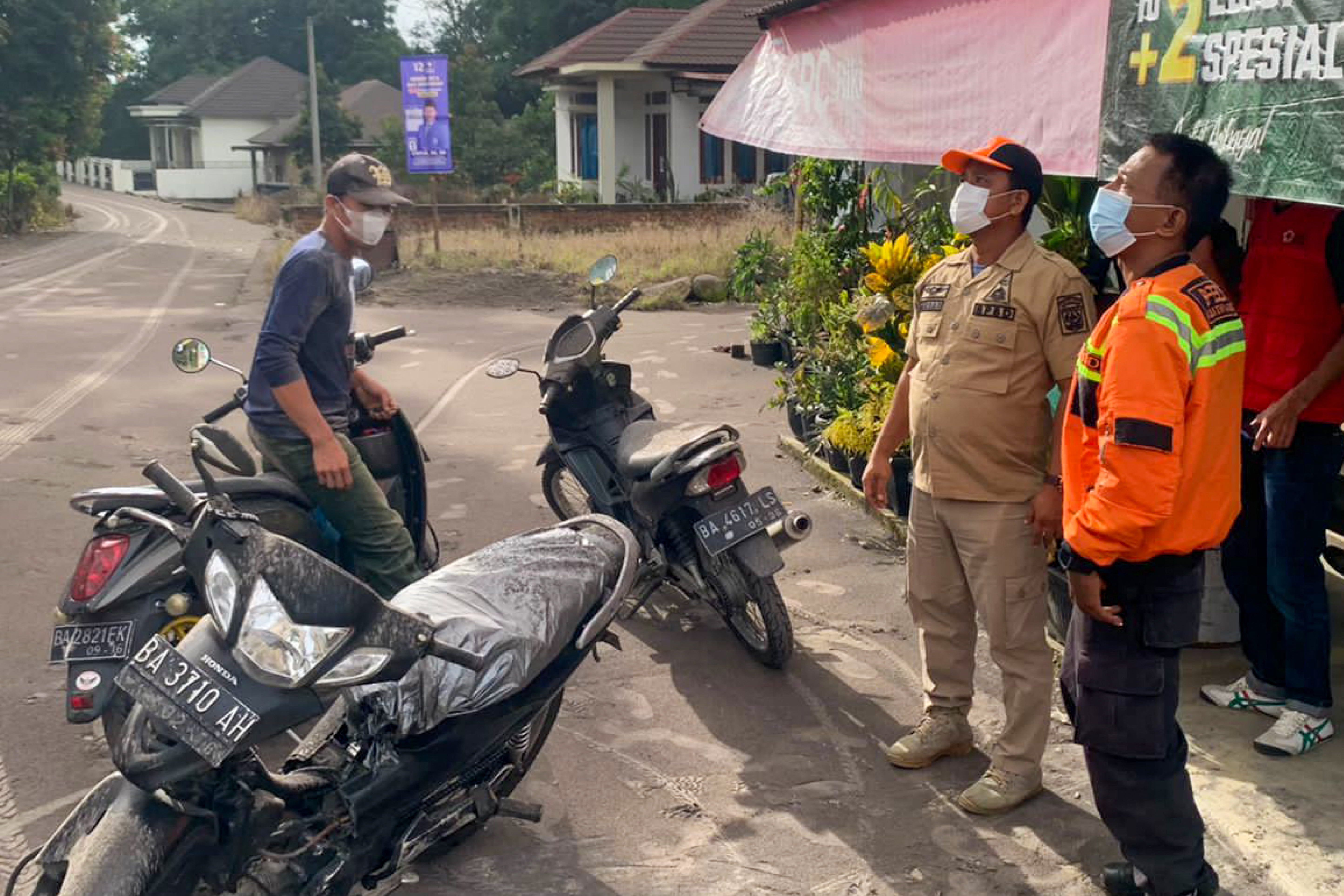 officials looking on as volcanic ash from the eruption of Mount Marapi on Sumatra island covers the village of Nagari Lasi