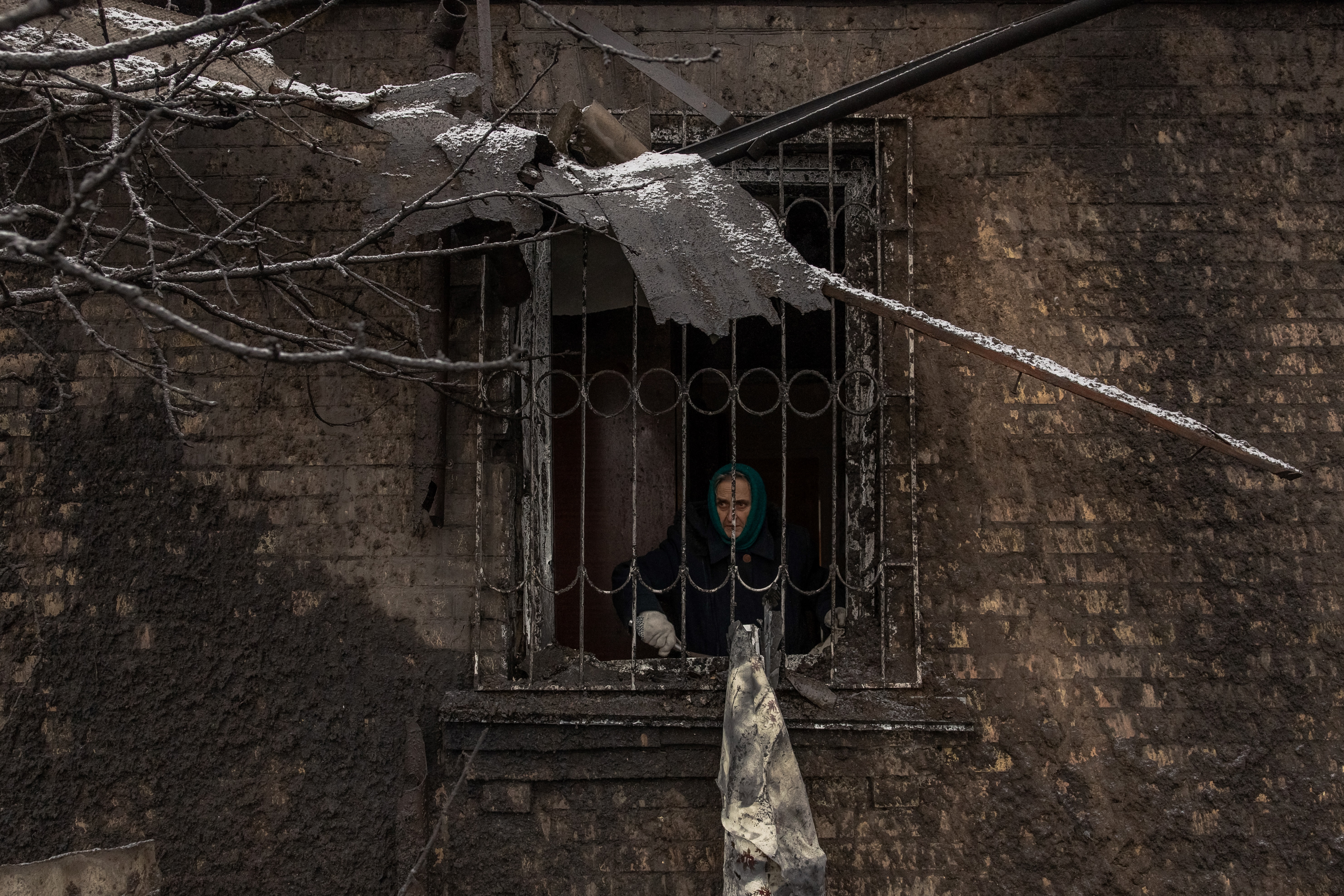 An elderly Ukrainian woman looking out from her house after it was damaged in a Russian attack