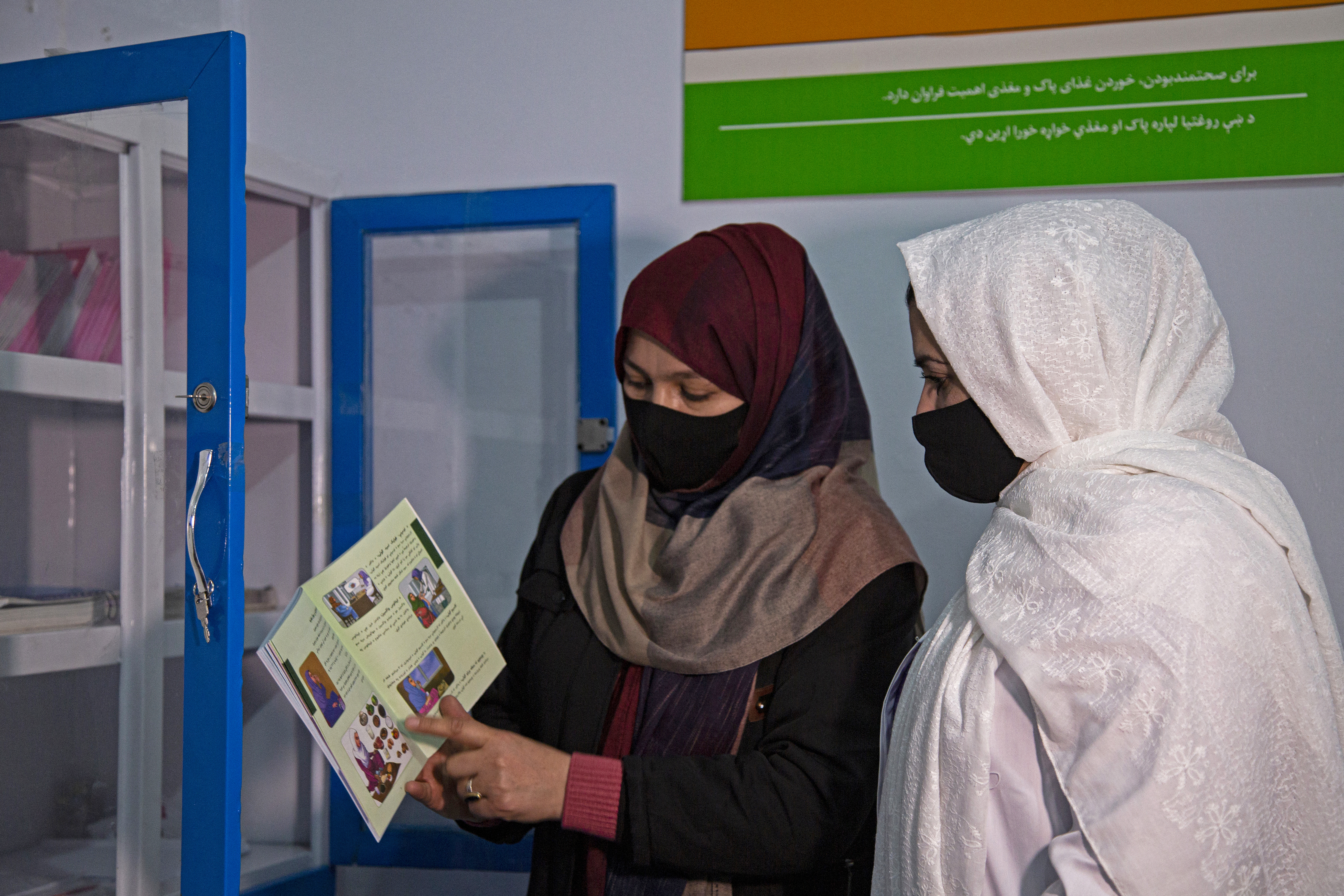 In this photograph taken on December 7, 2023, Momina Kohistani (L), head midwife at Norwegian Afghanistan Committee (NAC)-run Comprehensive-Continuum of Care Centre, a maternity hospital, shows a catalogue to fellow midwife Zainab Dawlatzai, in the facility at Gardez, the capital of Afghanistan's Paktia province.